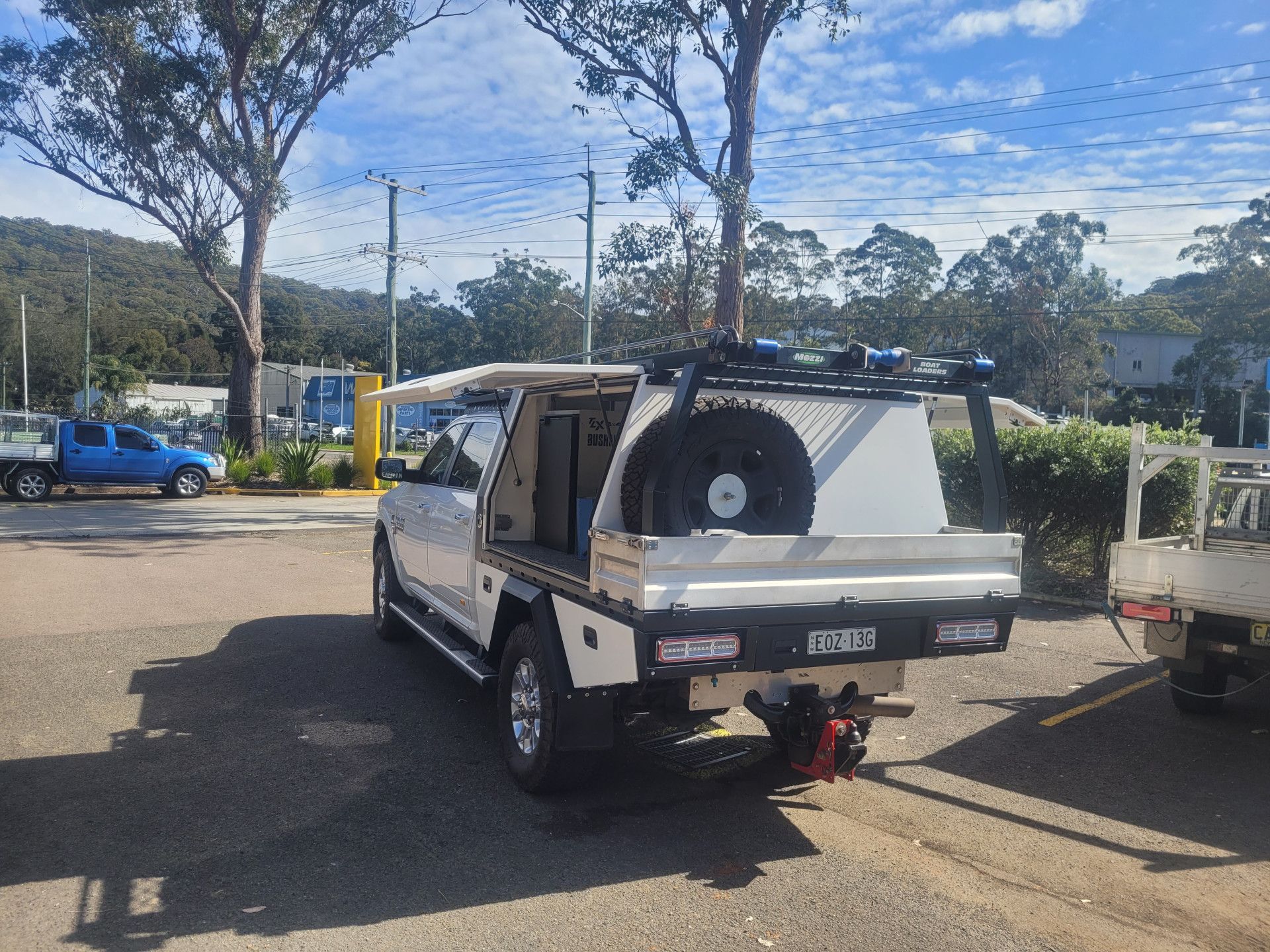A white utility truck with an open canopy and spare tire mounted on the rear, parked in an outdoor lot on a sunny day.