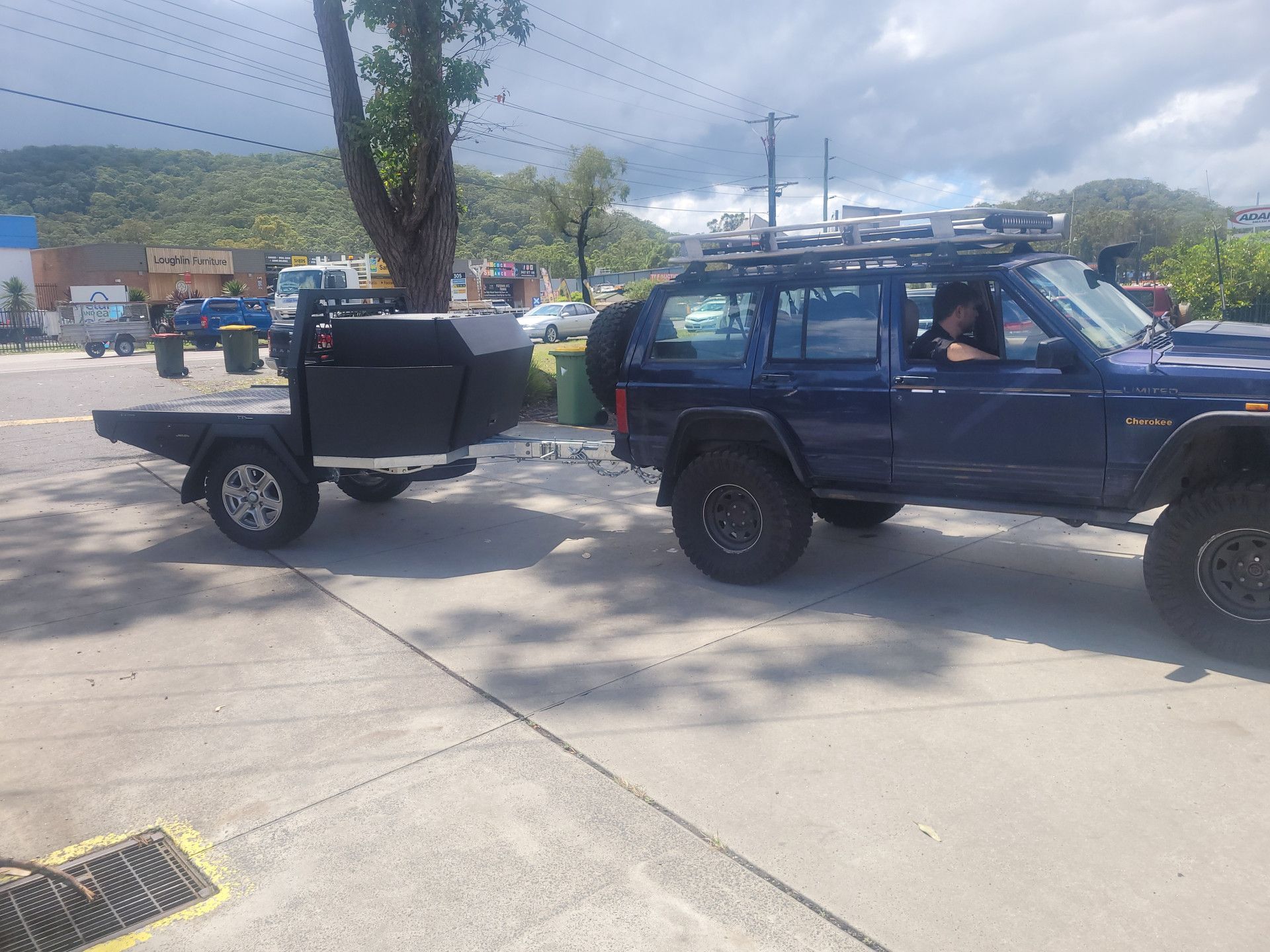 A dark blue SUV towing a black utility trailer on a paved lot with a mountainous landscape in the background.