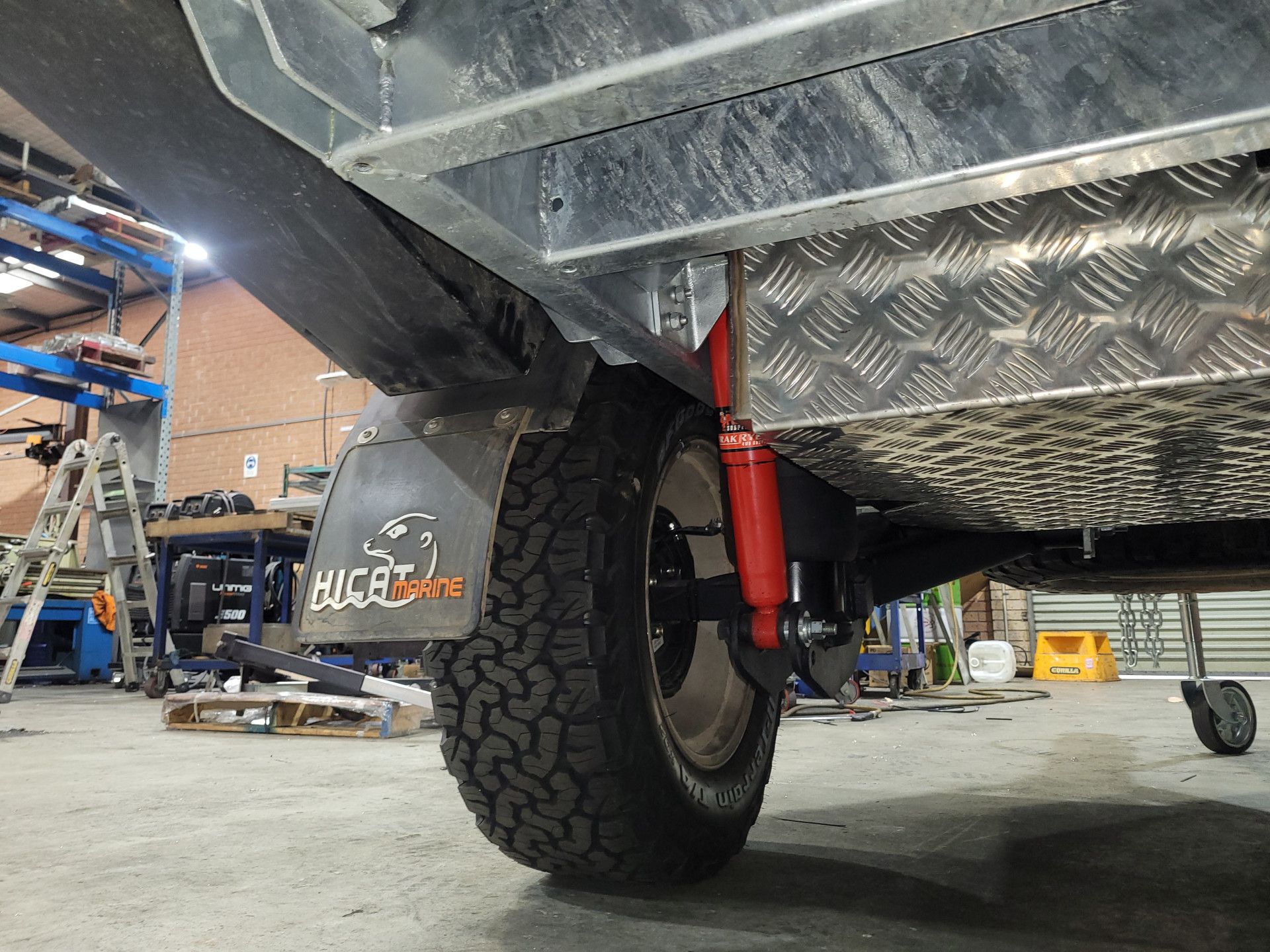 Close-up of a trailer's wheel, suspension system, and bright red shock absorber mounted beneath a metal chassis.