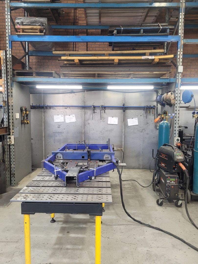 A Blue Metal Trailer Frame on A Large Steel Welding Table in A Workshop — Real Engineering in West Gosford, NSW