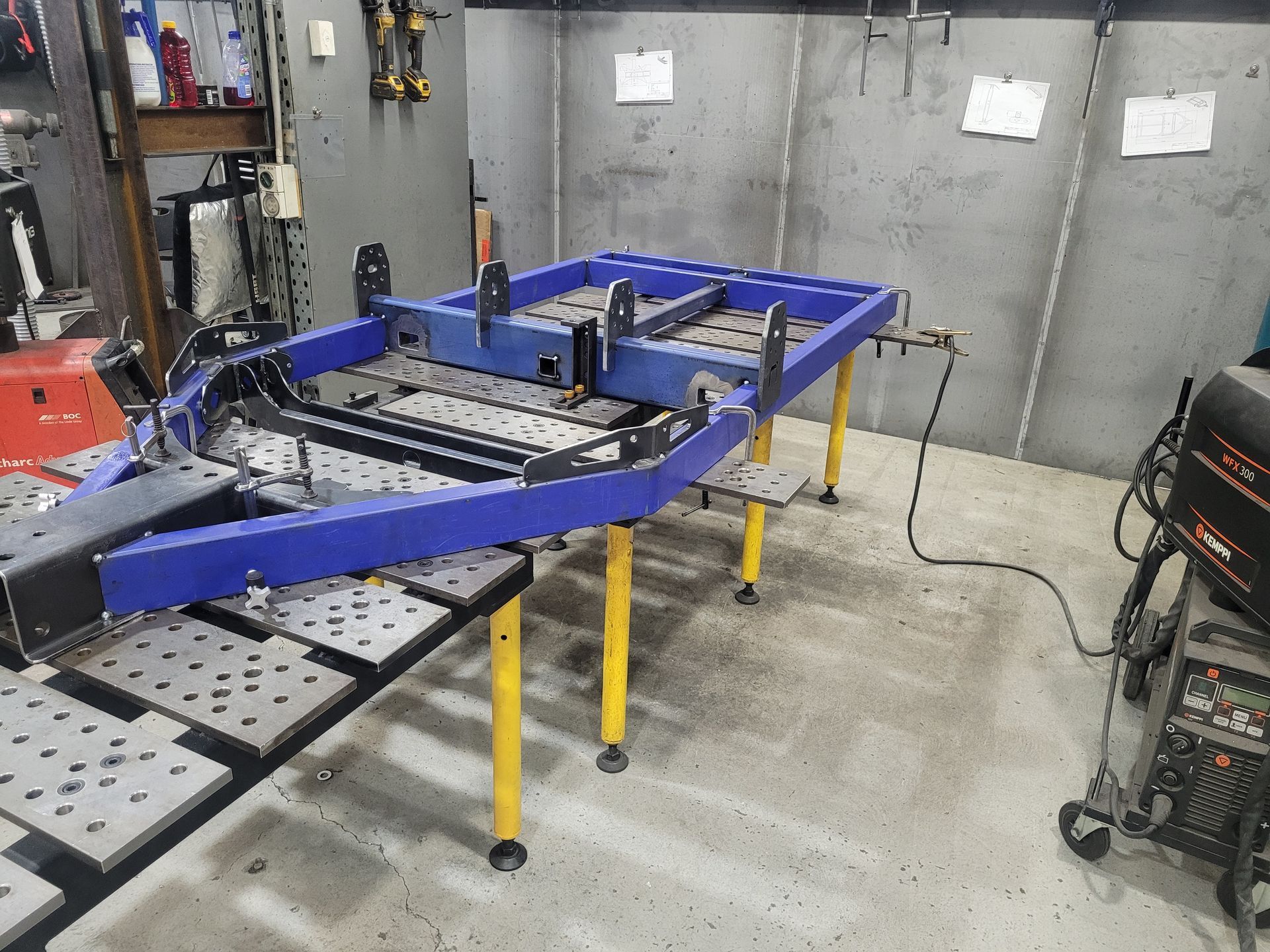 Blue car frame on yellow stands in a workshop with tools and machinery nearby — Real Engineering in Ingleburn, NSW