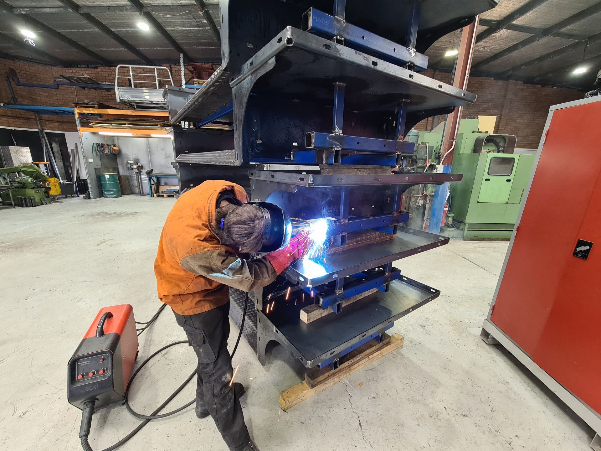 A Welder in Protective Orange Gear Uses a Welding Torch on A Large Metal Structure — Real Engineering in West Gosford, NSW