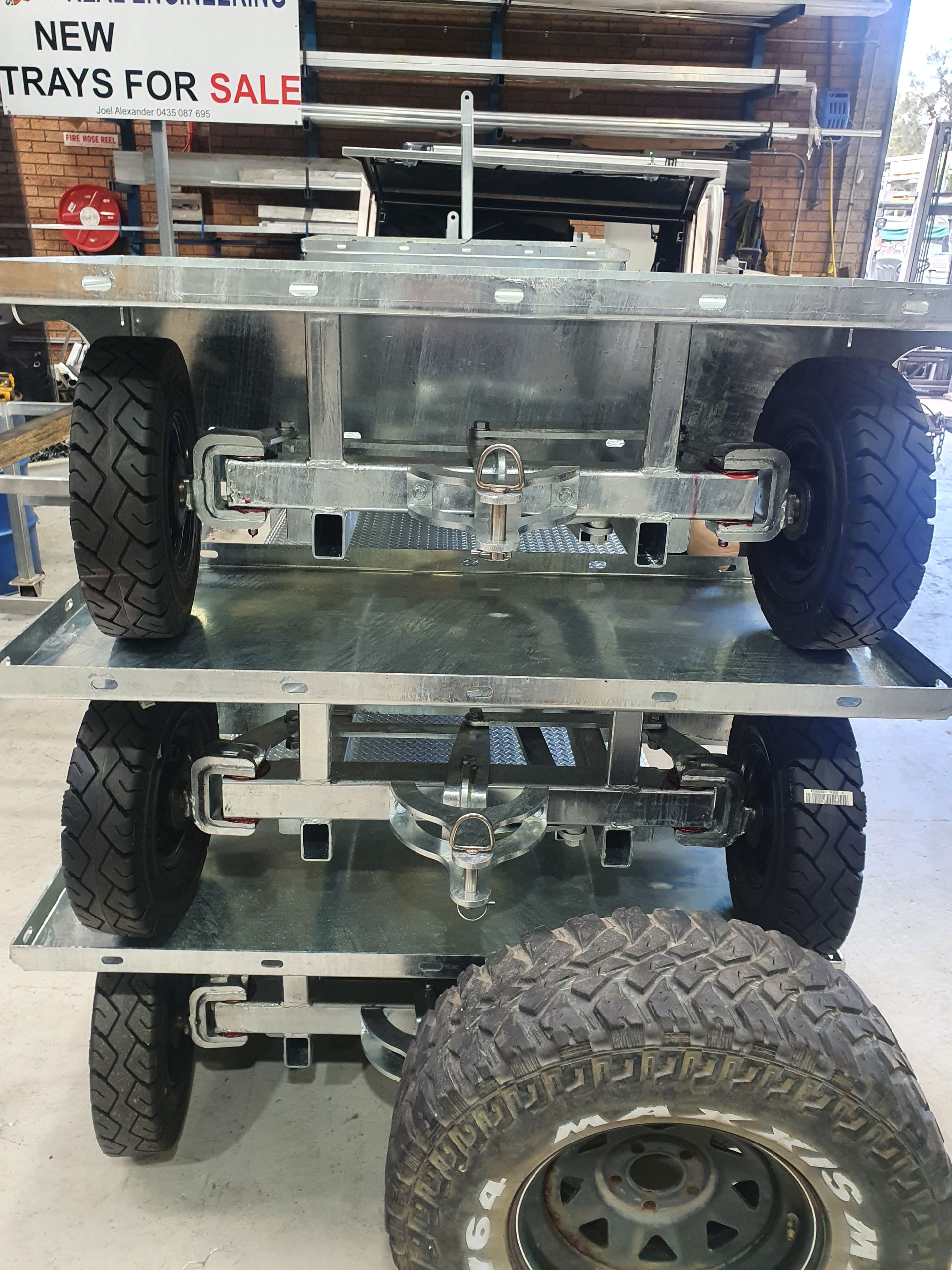 Stacked galvanized metal trailer trays for sale, with wheels and a spare tire visible in an indoor shop setting.