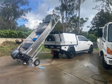 A small aluminum boat on a trailer tilted vertically behind a white pickup truck on a paved outdoor lot.