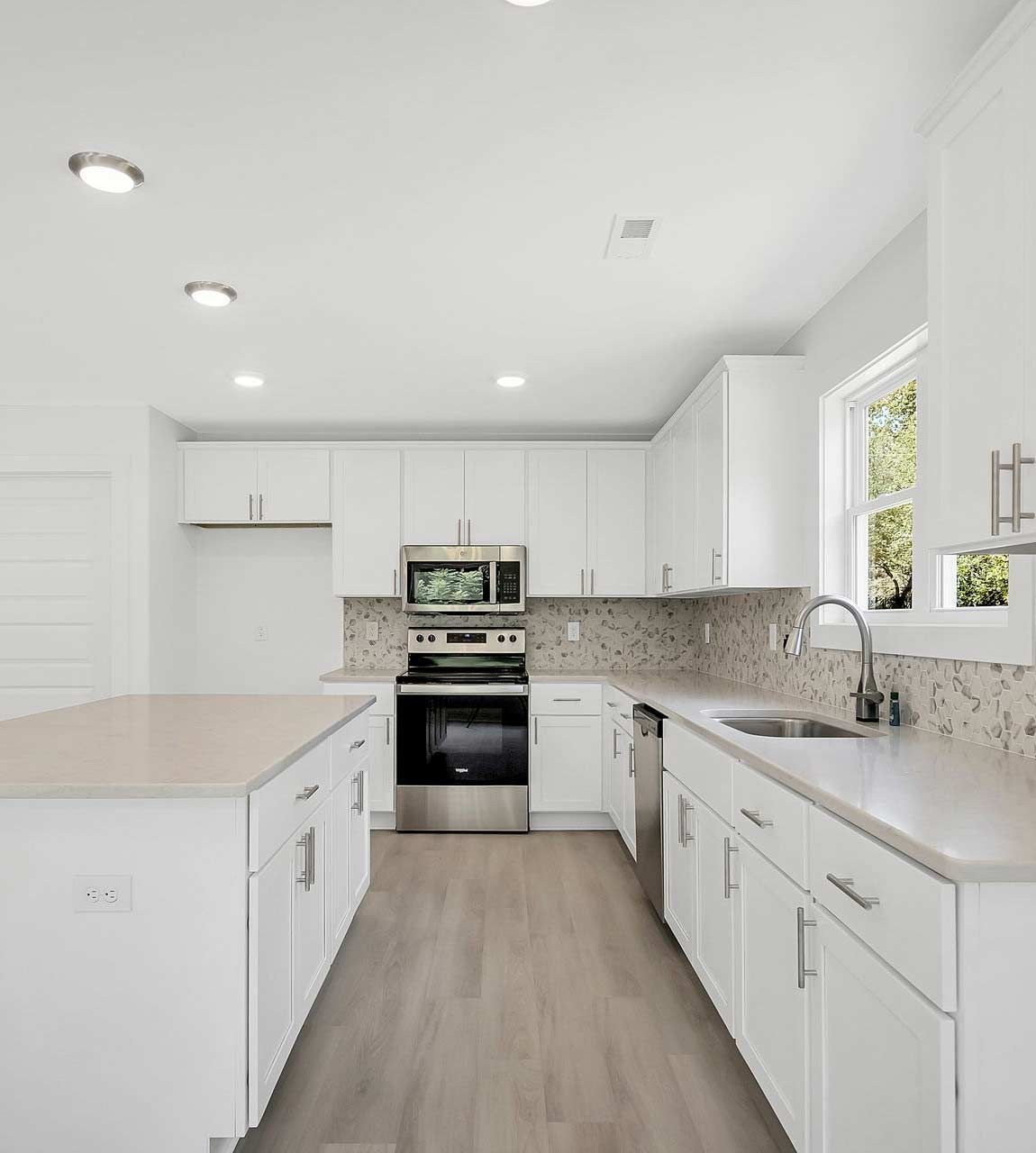 A modern, bright kitchen featuring white cabinets, stainless steel appliances, a center island, and wood-look flooring.
