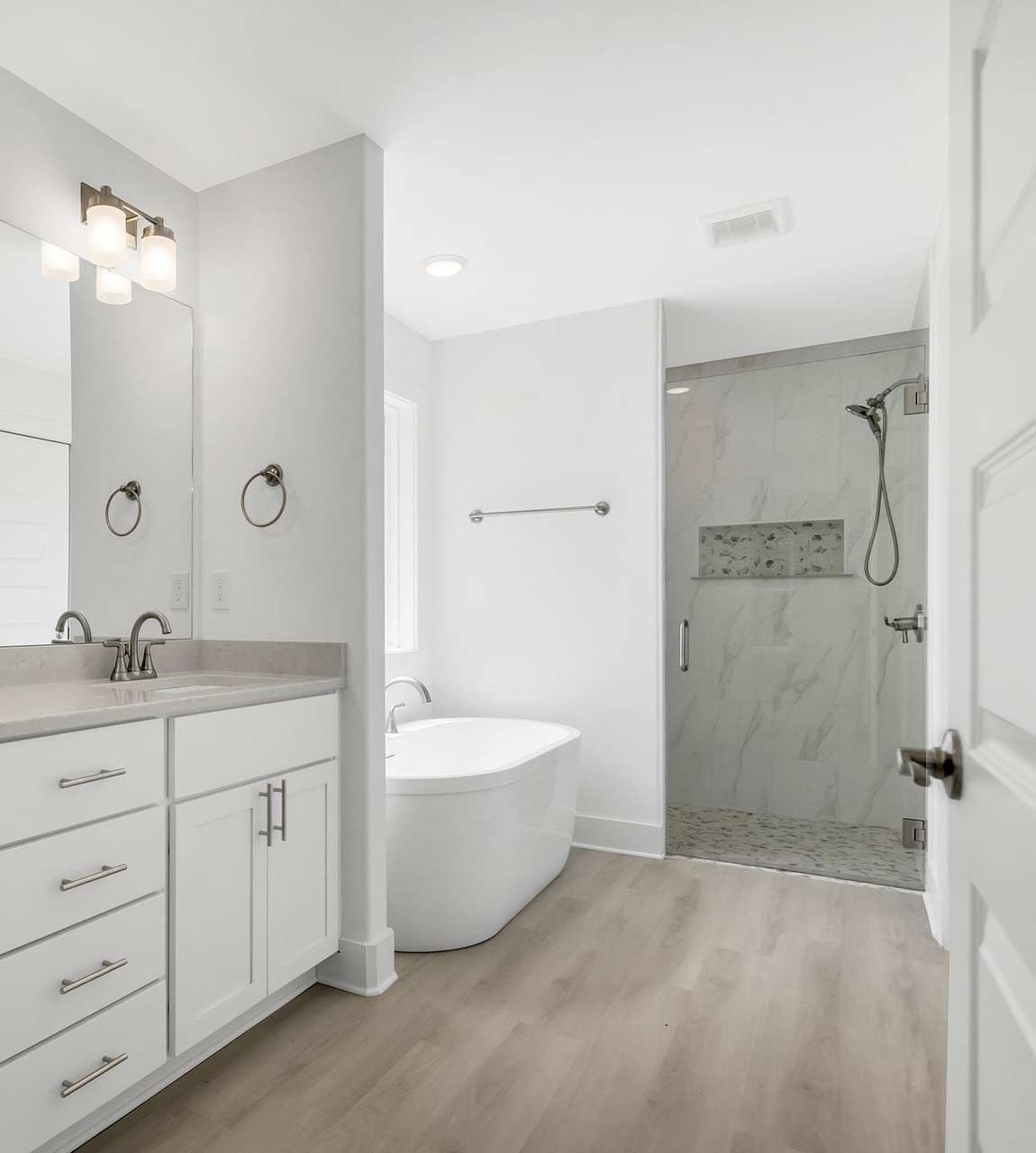 A modern white bathroom with a double vanity, a freestanding tub, and a glass-enclosed walk-in shower.