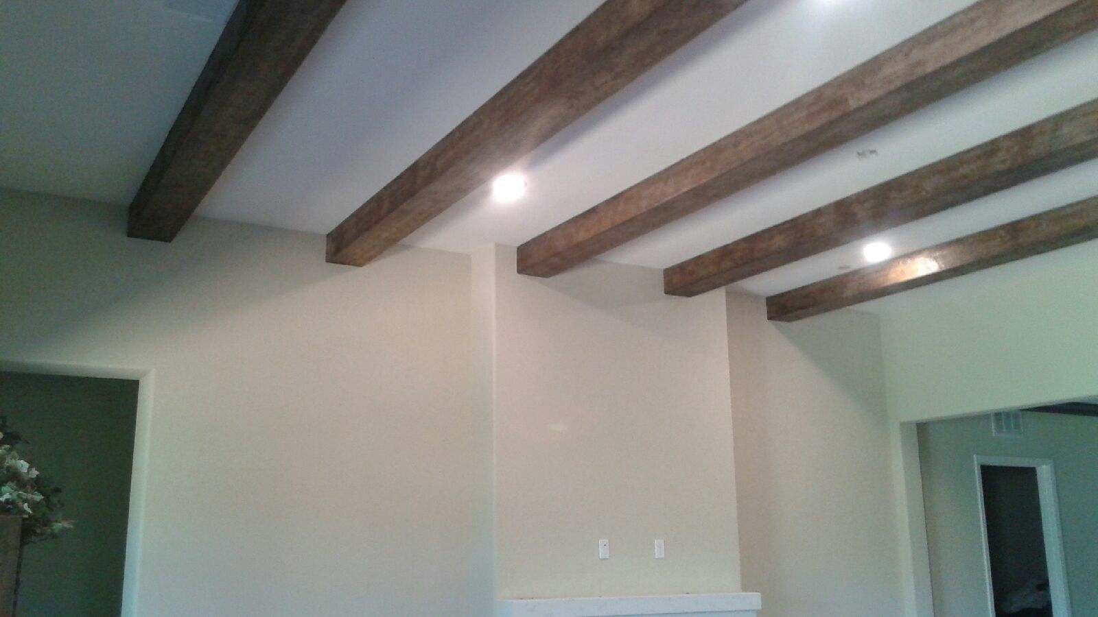Beamed ceiling with recessed lighting. Wooden beams are brown against a white ceiling. Beige walls.