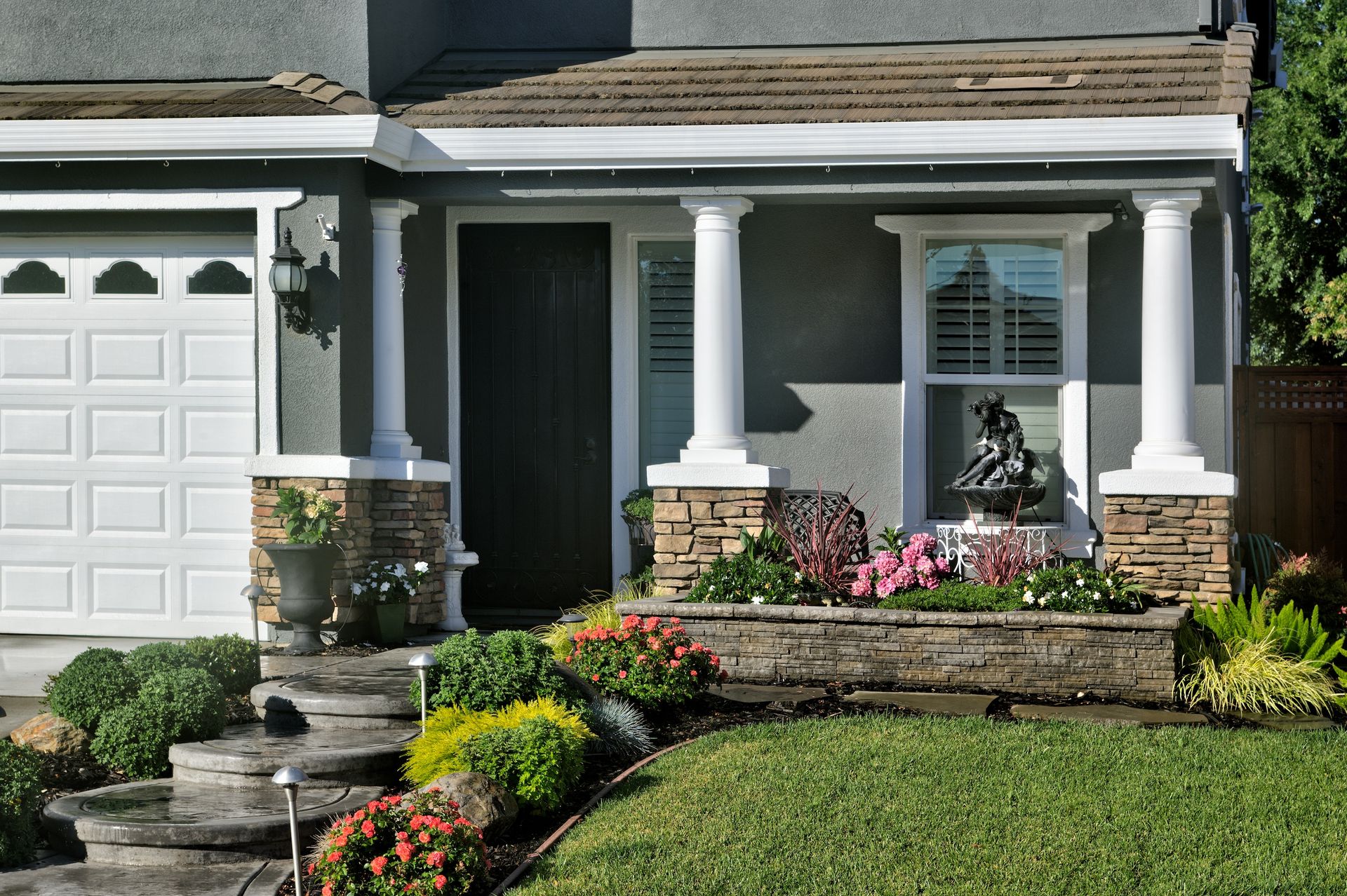 Gray house with white pillars, front door, garage, and flower beds.