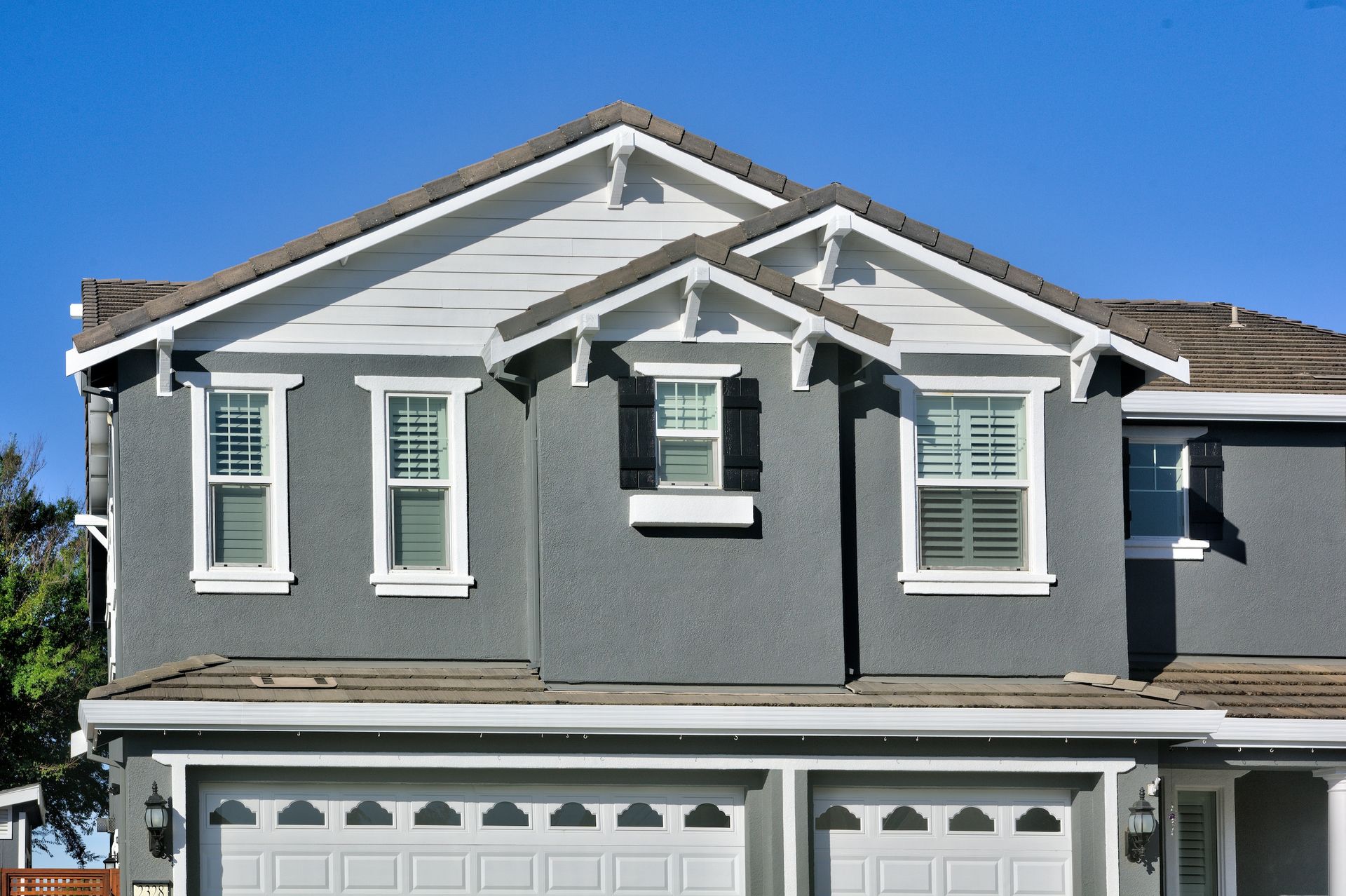 Gray house with white trim and garage doors against a blue sky.