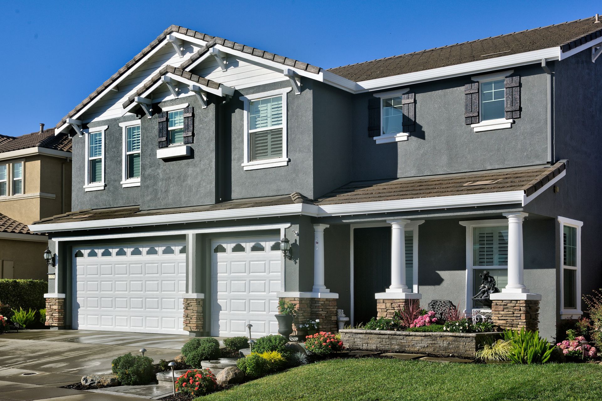 Two-story gray house with white trim, a porch, and a two-car garage on a sunny day.