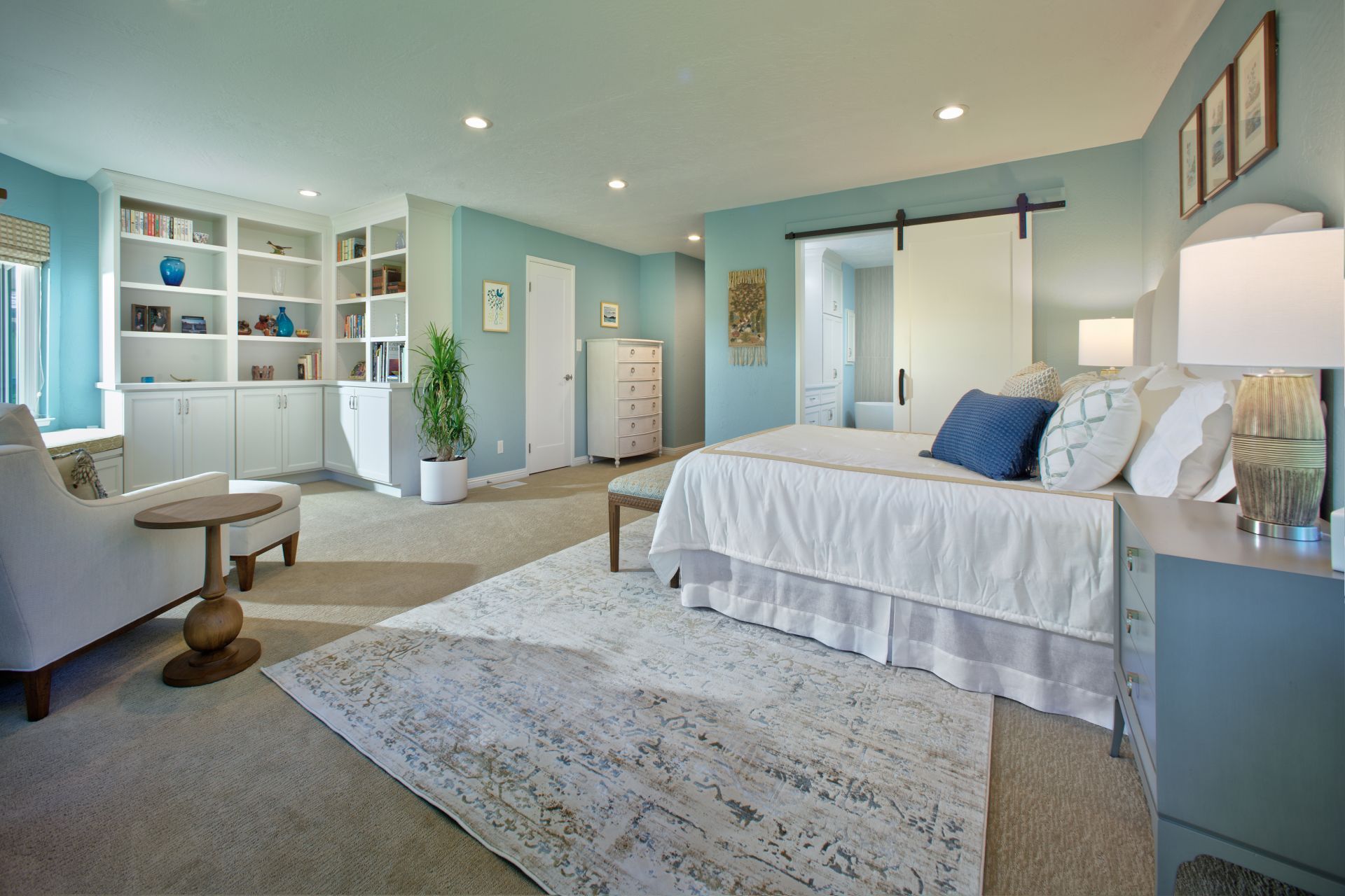 Spacious, light blue bedroom with a large bed, built-in bookshelves, and a cozy reading nook.