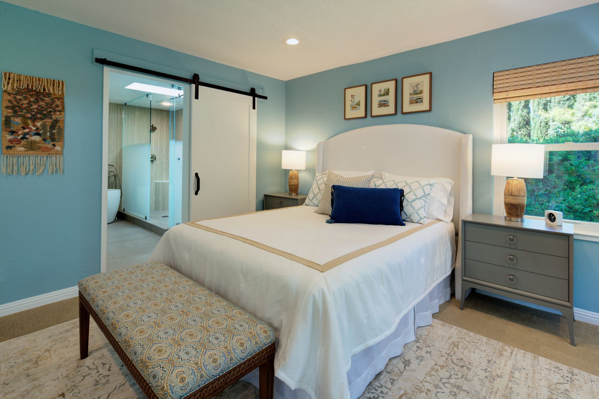 Bedroom with a white bed, blue walls, and a sliding barn door to a bathroom.