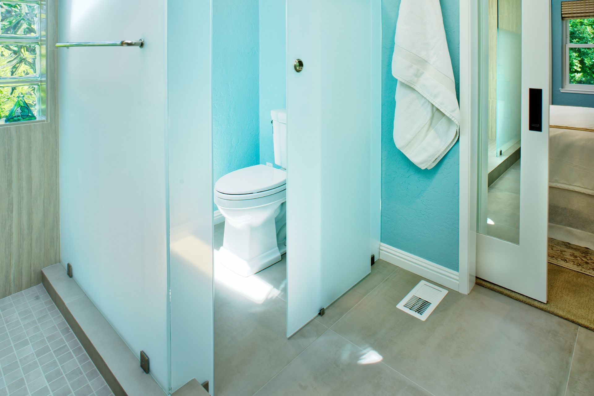 Modern bathroom with a toilet enclosed by frosted glass walls and a light blue wall.