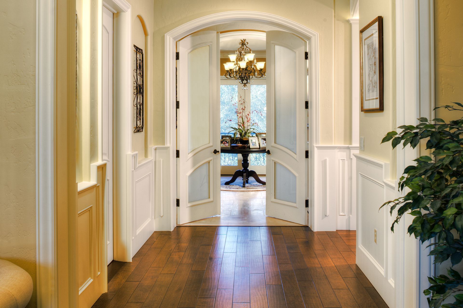 Hallway with hardwood floors, white paneled walls, and double doors leading to a dining room.