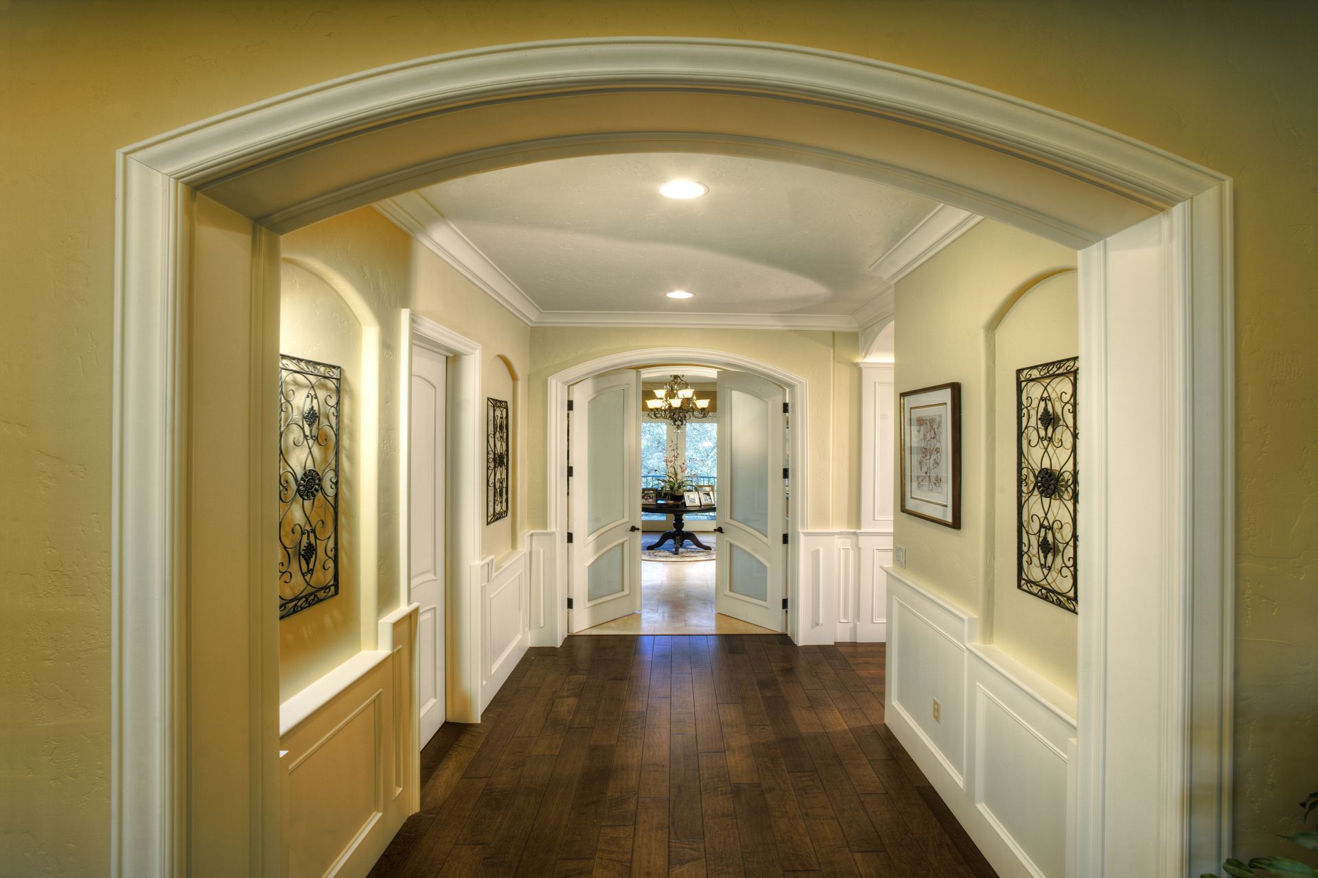 Hallway with arched doorways, wood floor, and white trim; light yellow walls and decorative iron wall art.