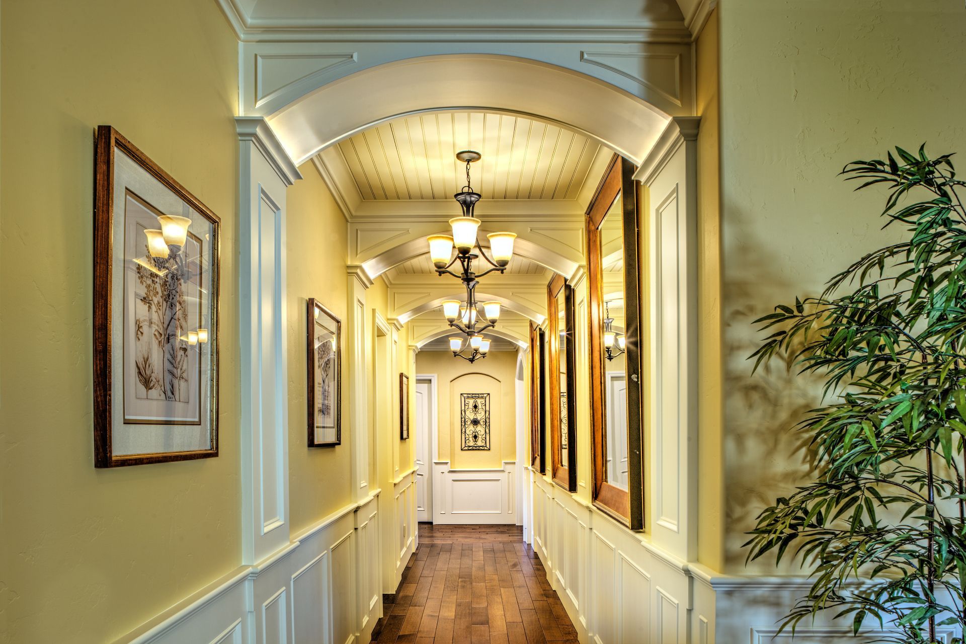 Hallway with arched doorways, artwork, mirrors, and a potted plant.
