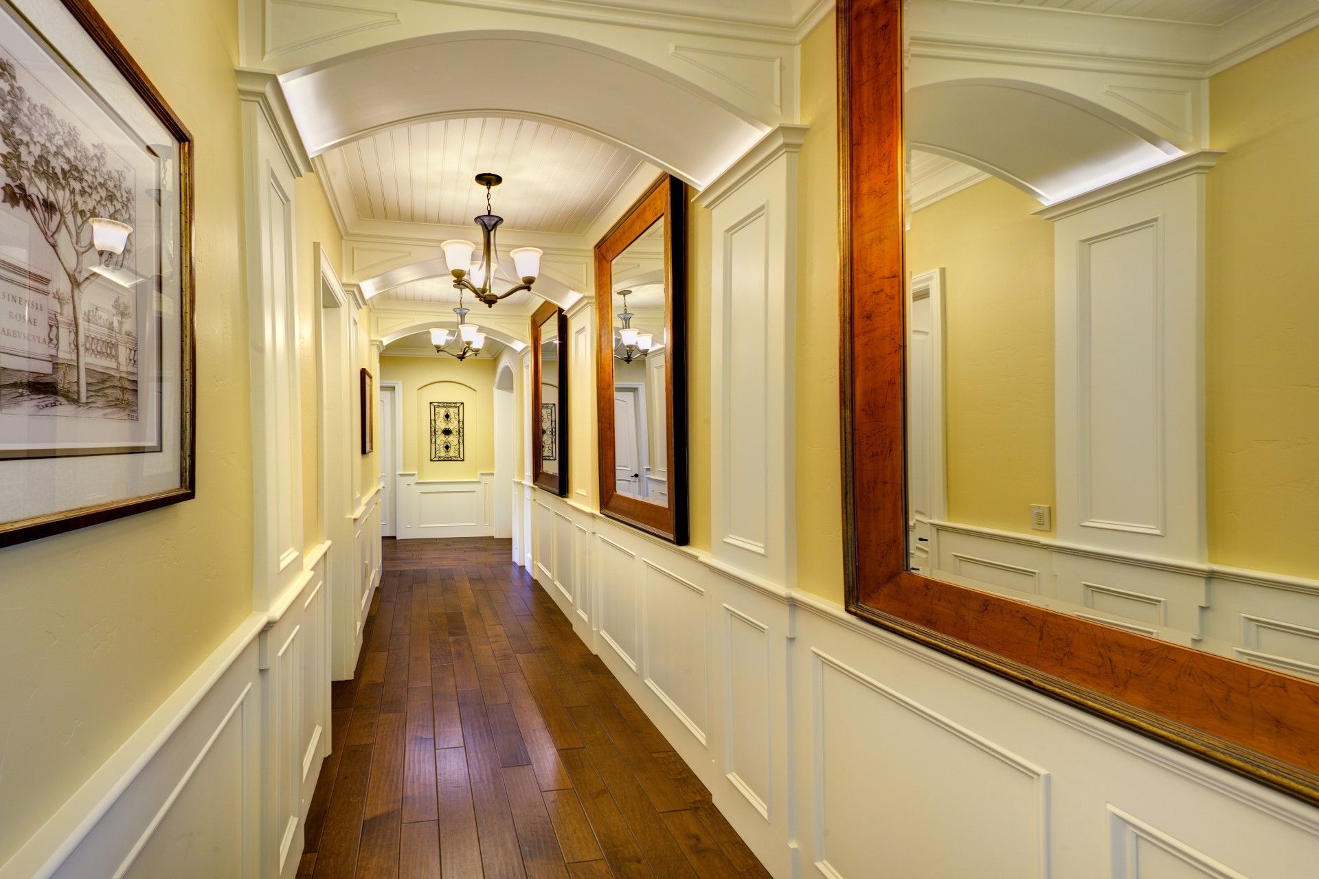 Long hallway with wood floors, yellow walls, and large mirrors.