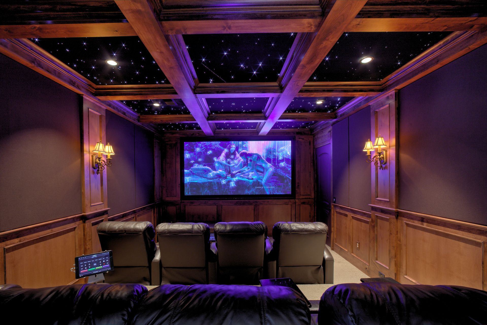 Home theater with screen, recliners, star ceiling, and wood paneling bathed in purple light.