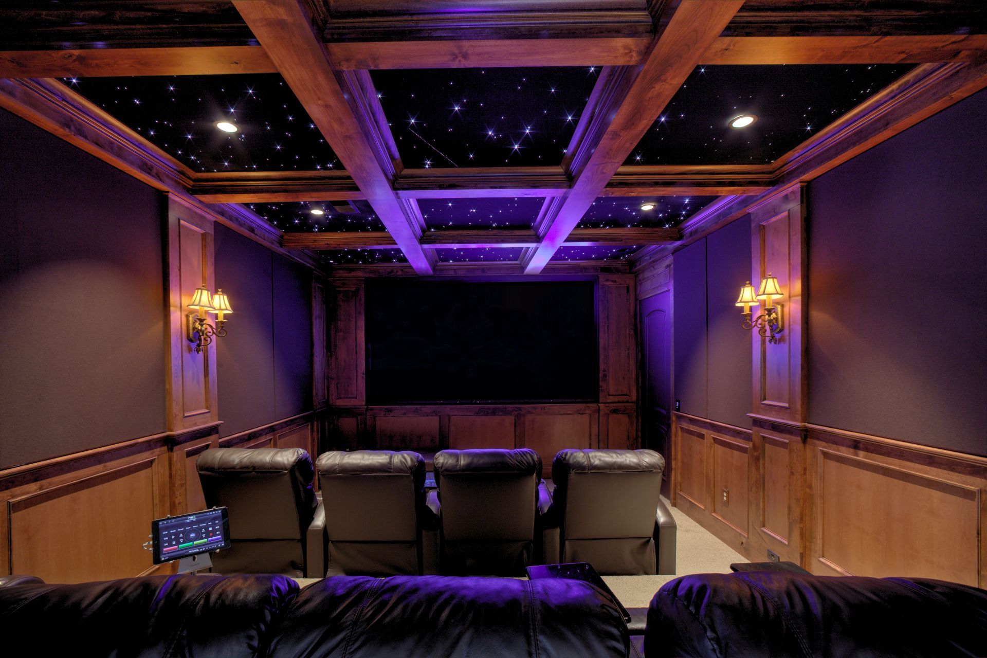 Home theater with starry ceiling, dark screen, leather seating, and wood paneling illuminated with purple lighting.