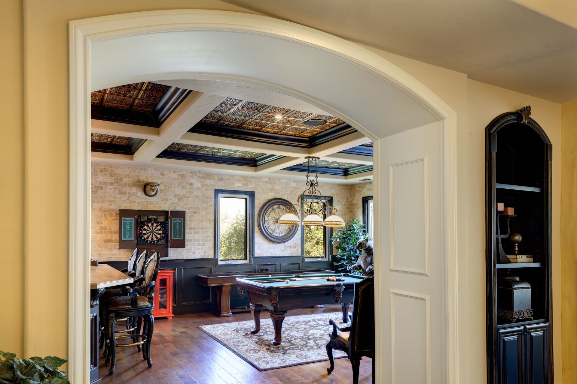 Archway into a game room with a pool table, dartboard, and ornate ceiling.