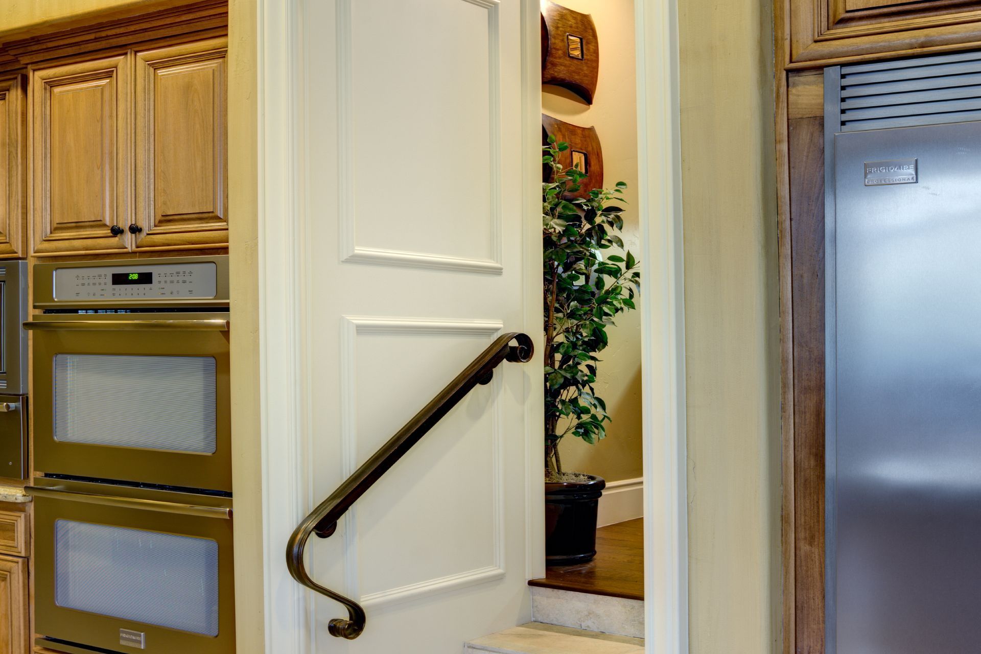 White door with a handrail leading to a staircase in a kitchen. Cabinets and oven are visible.