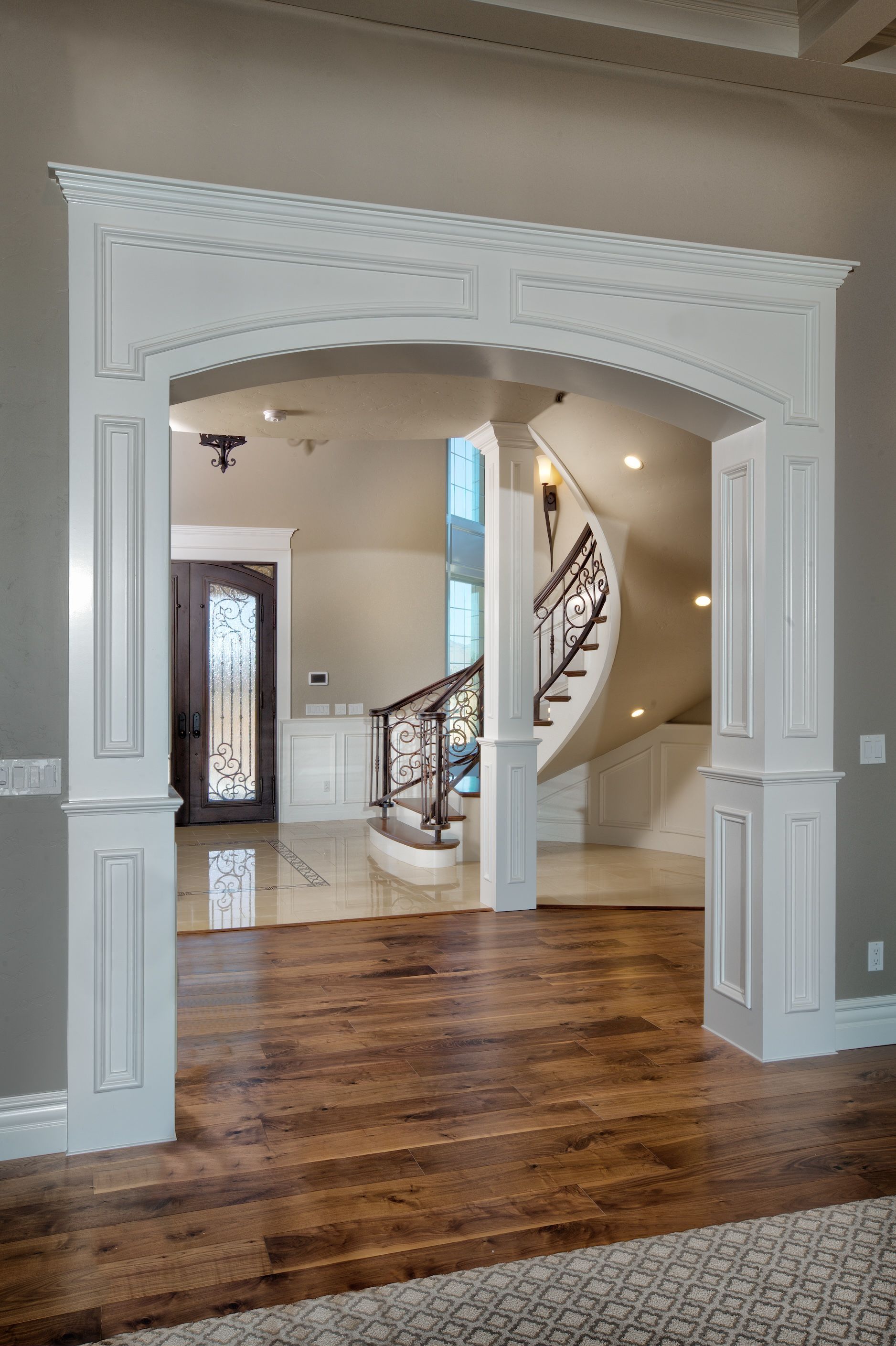 White arched doorway leads to a grand foyer with a winding staircase and wood flooring.