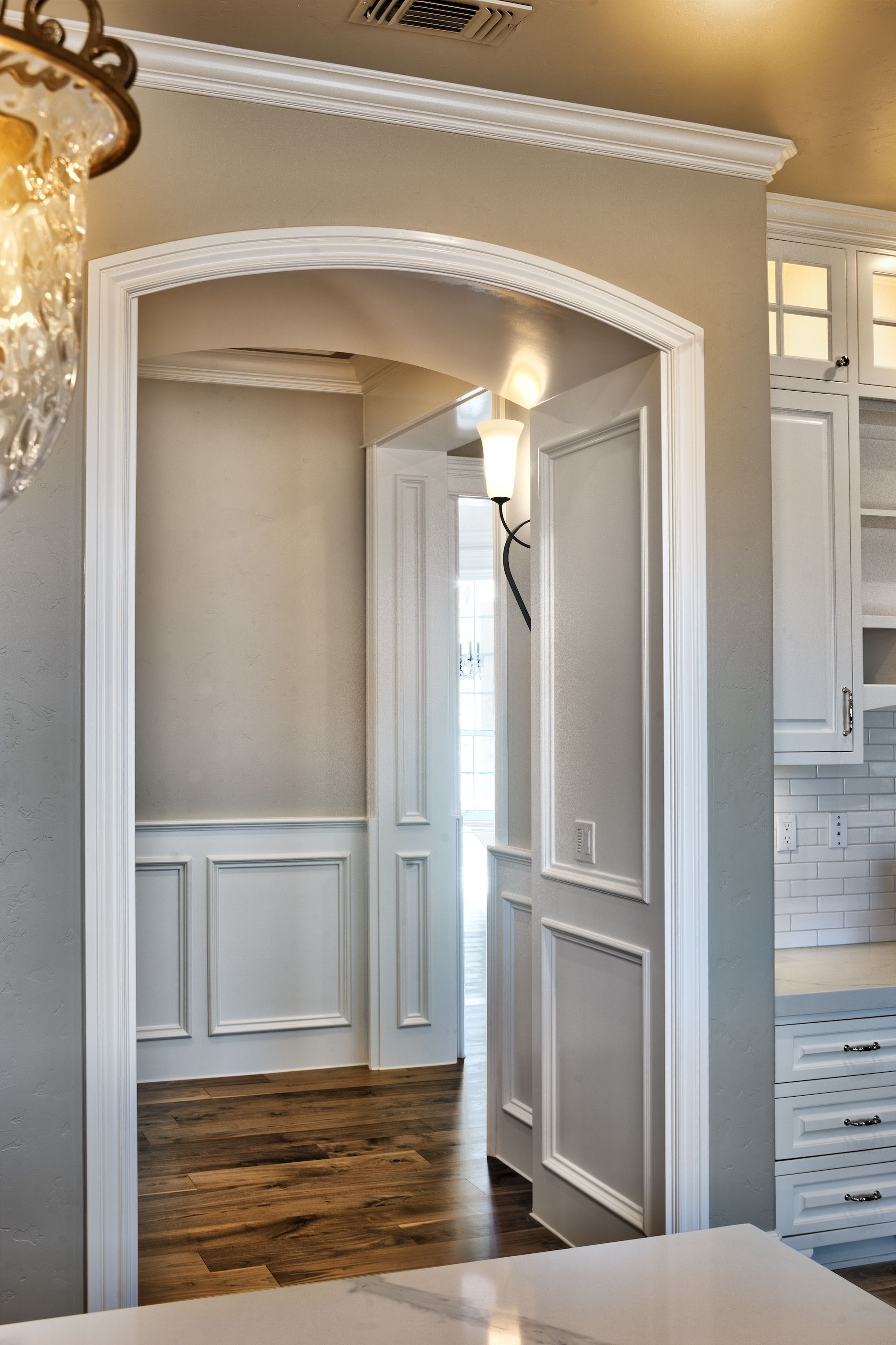 Archway leading to a hallway with white trim, molding, and paneling. Beige walls, dark wood floor.