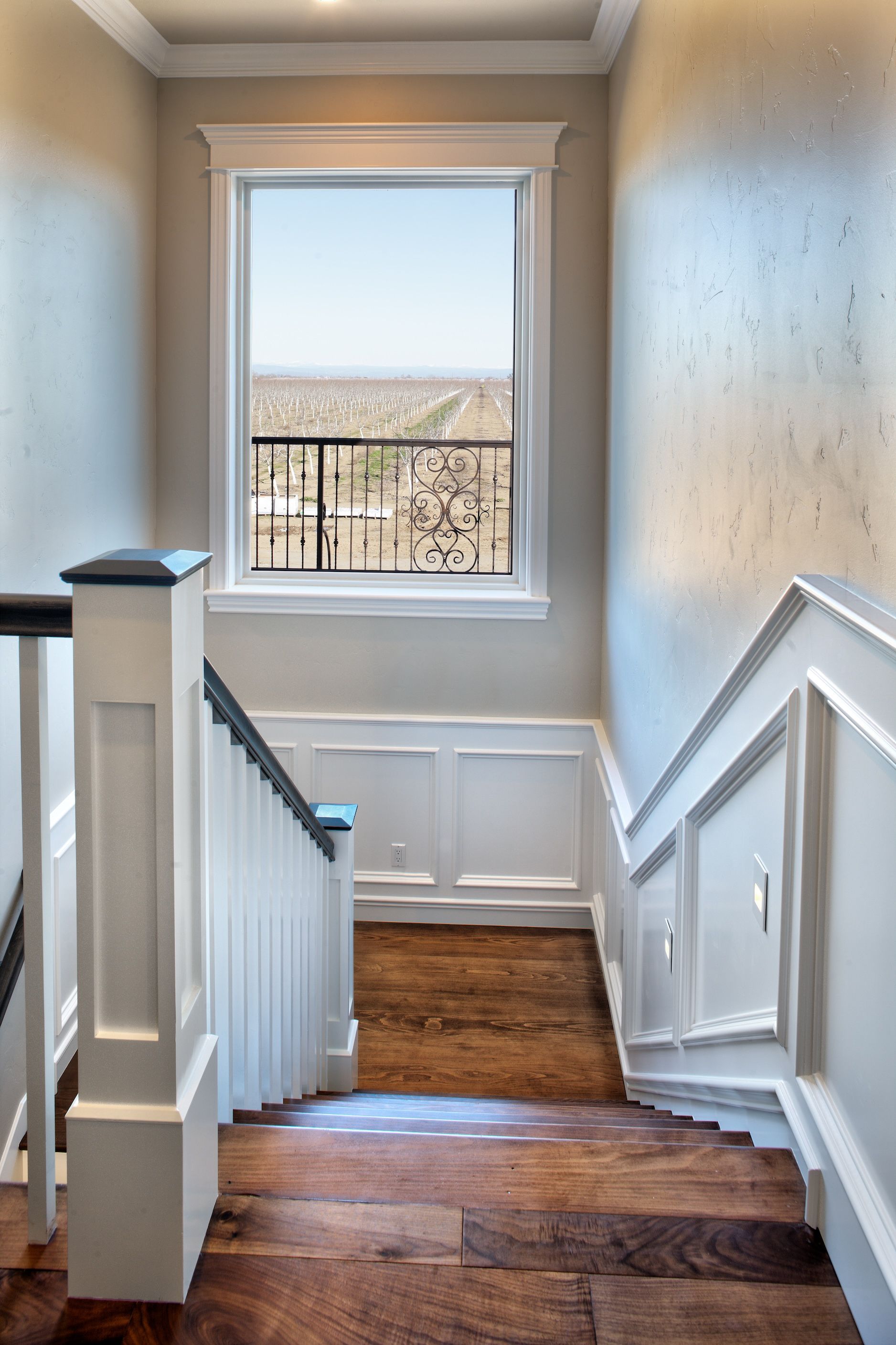 Stairwell with hardwood steps, white paneling, and a window overlooking a distant view.
