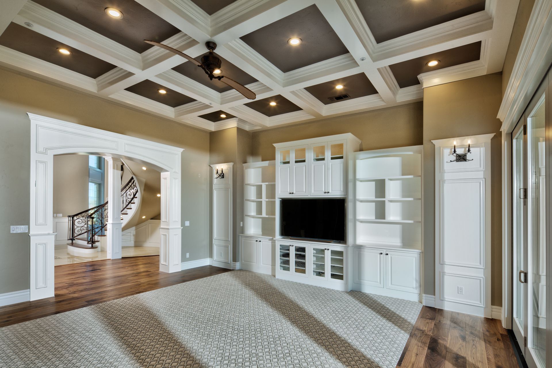 Living room with white built-ins, ceiling beams, and a view of a spiral staircase.