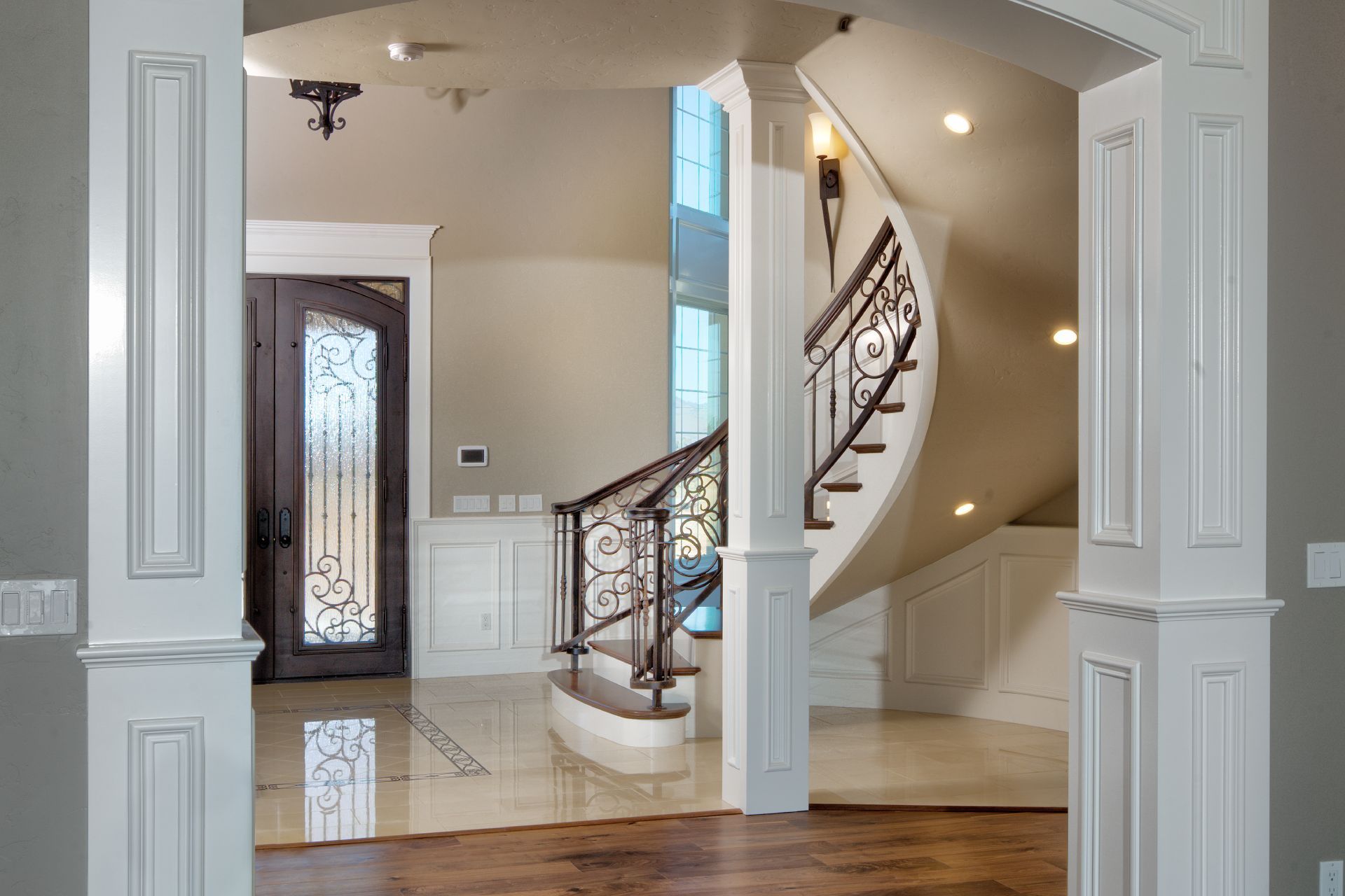 Elegant foyer with a curved staircase, ornate railing, and stained-glass door.