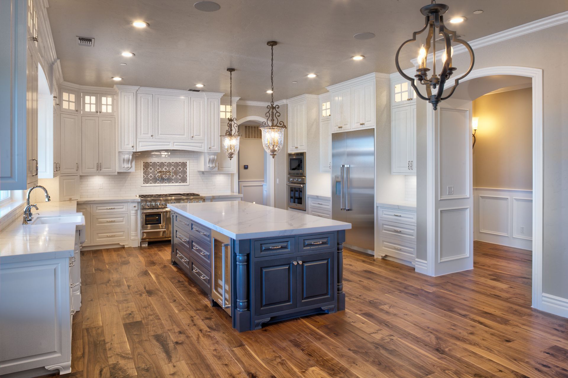 Spacious kitchen with white cabinets, blue island, stainless steel appliances, and hardwood floors.