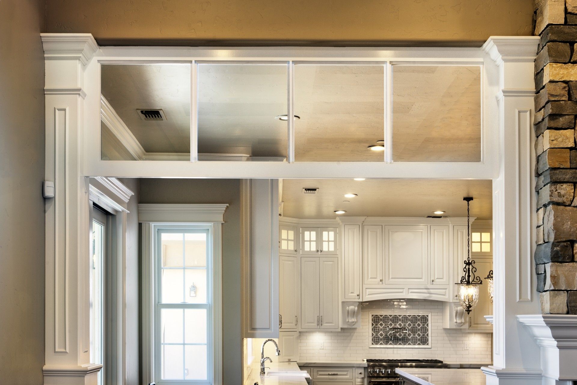 White kitchen doorway with glass panes above, white cabinets, and stone accent wall.