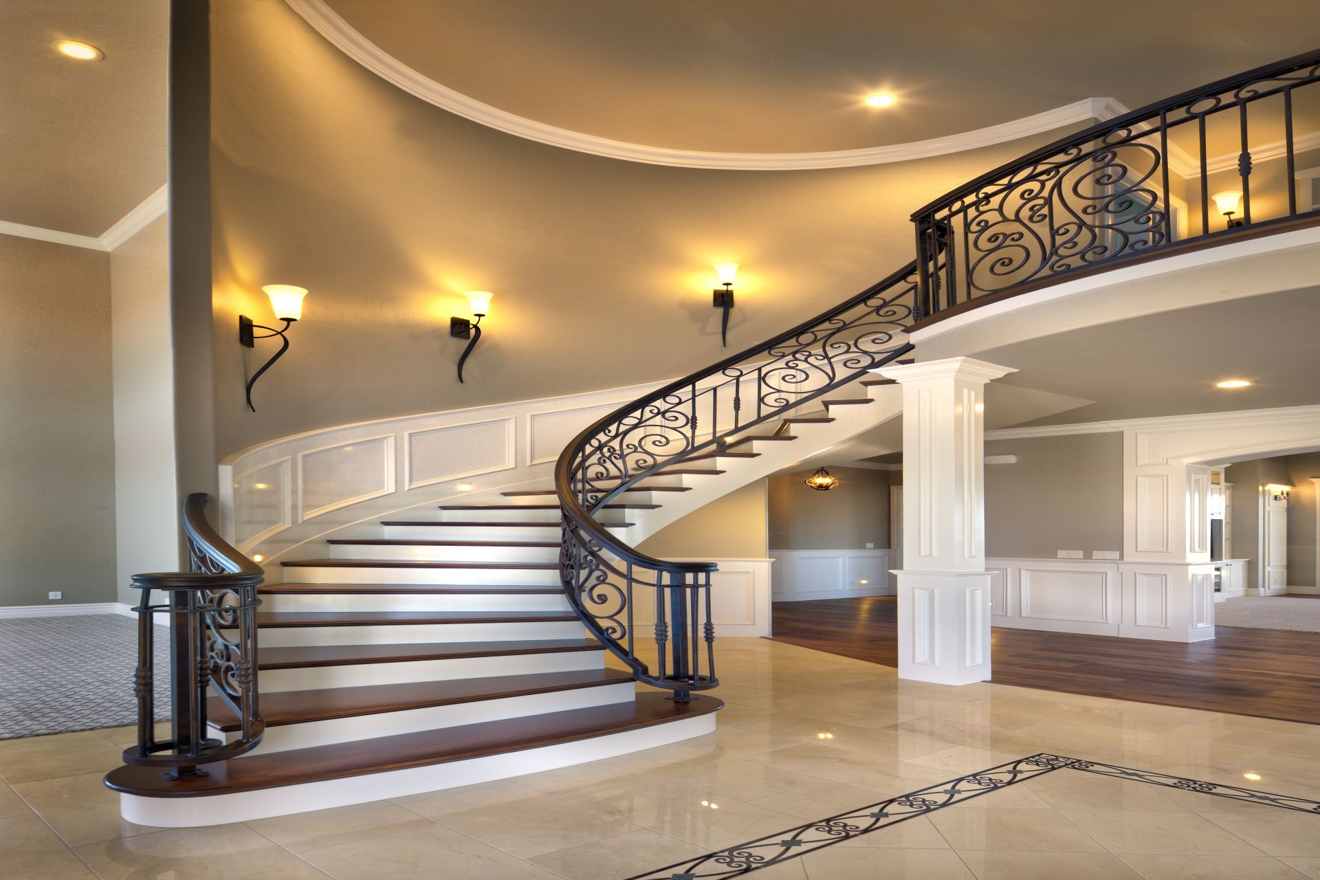 Elegant curved staircase with wrought iron railing in a grand, open foyer.