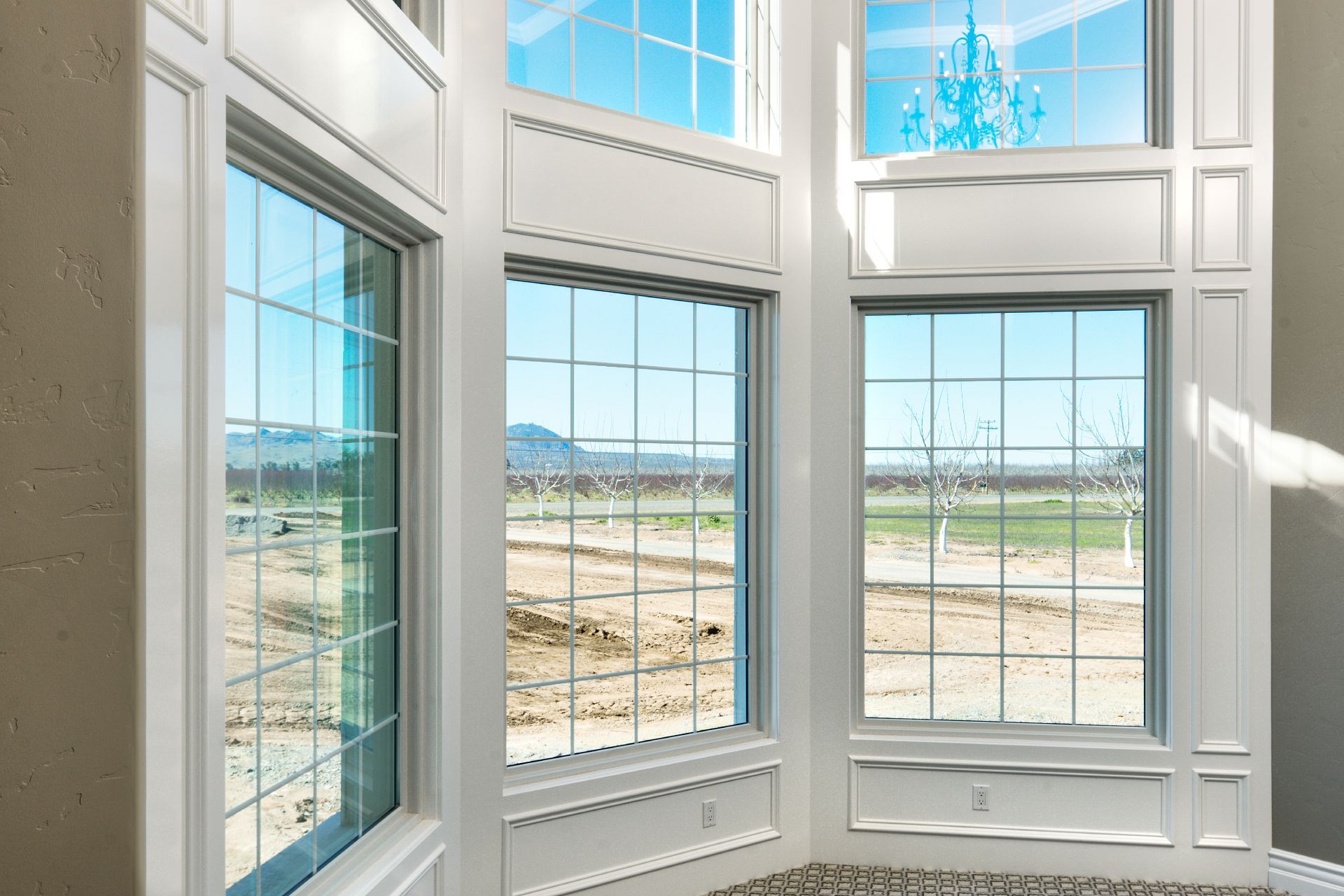 Interior view of large white framed windows overlooking a field and blue sky.