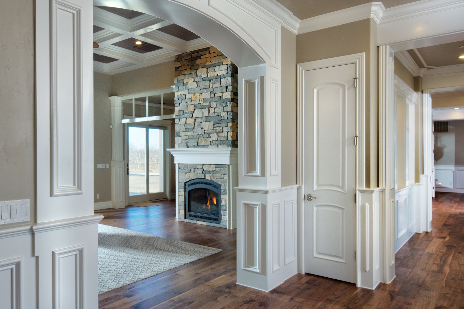 Interior view: archway, stone fireplace, white paneled walls, wood floors, light-filled space.