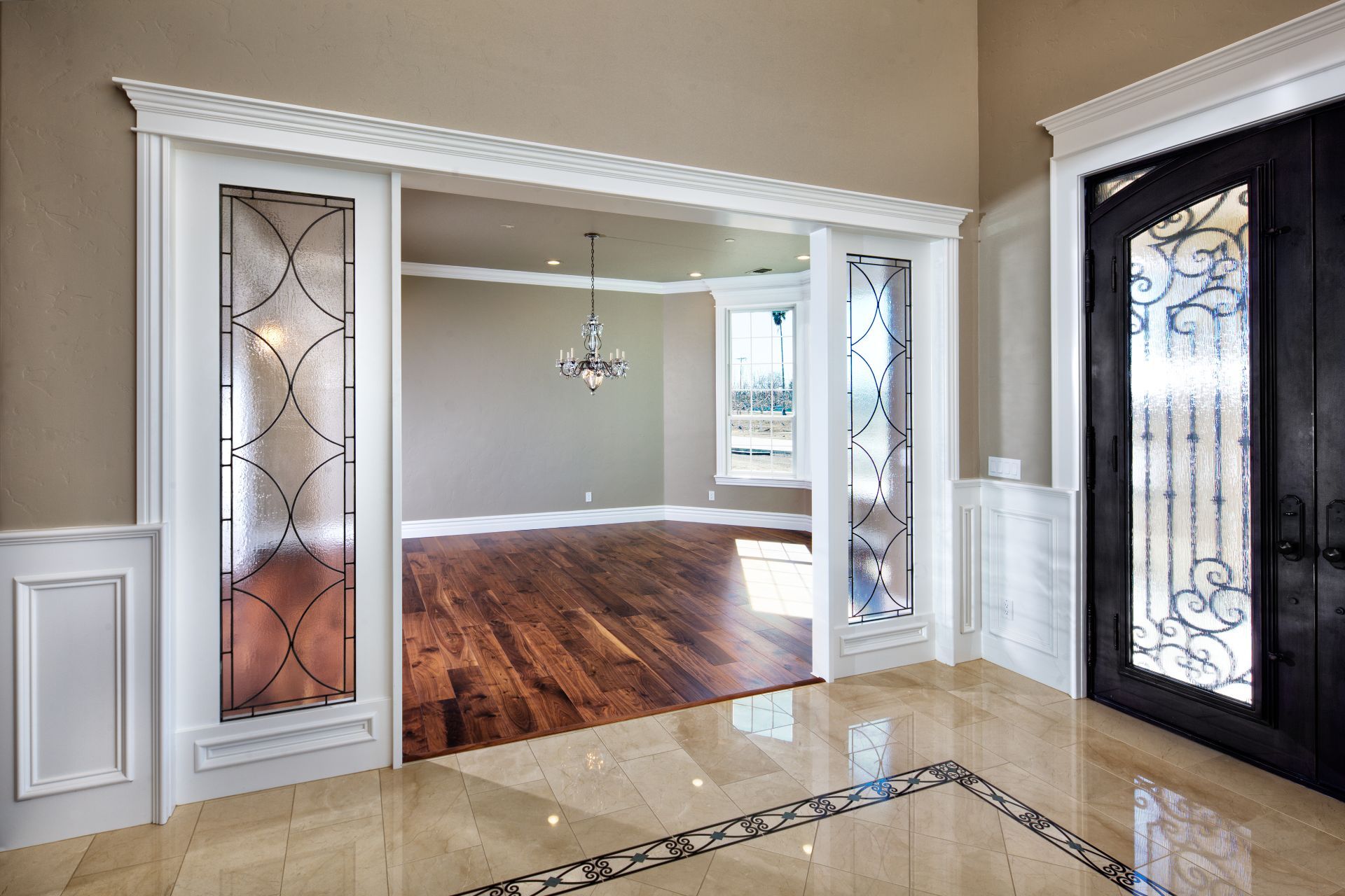 Elegant foyer with decorative glass doors leading to a room with hardwood floors.
