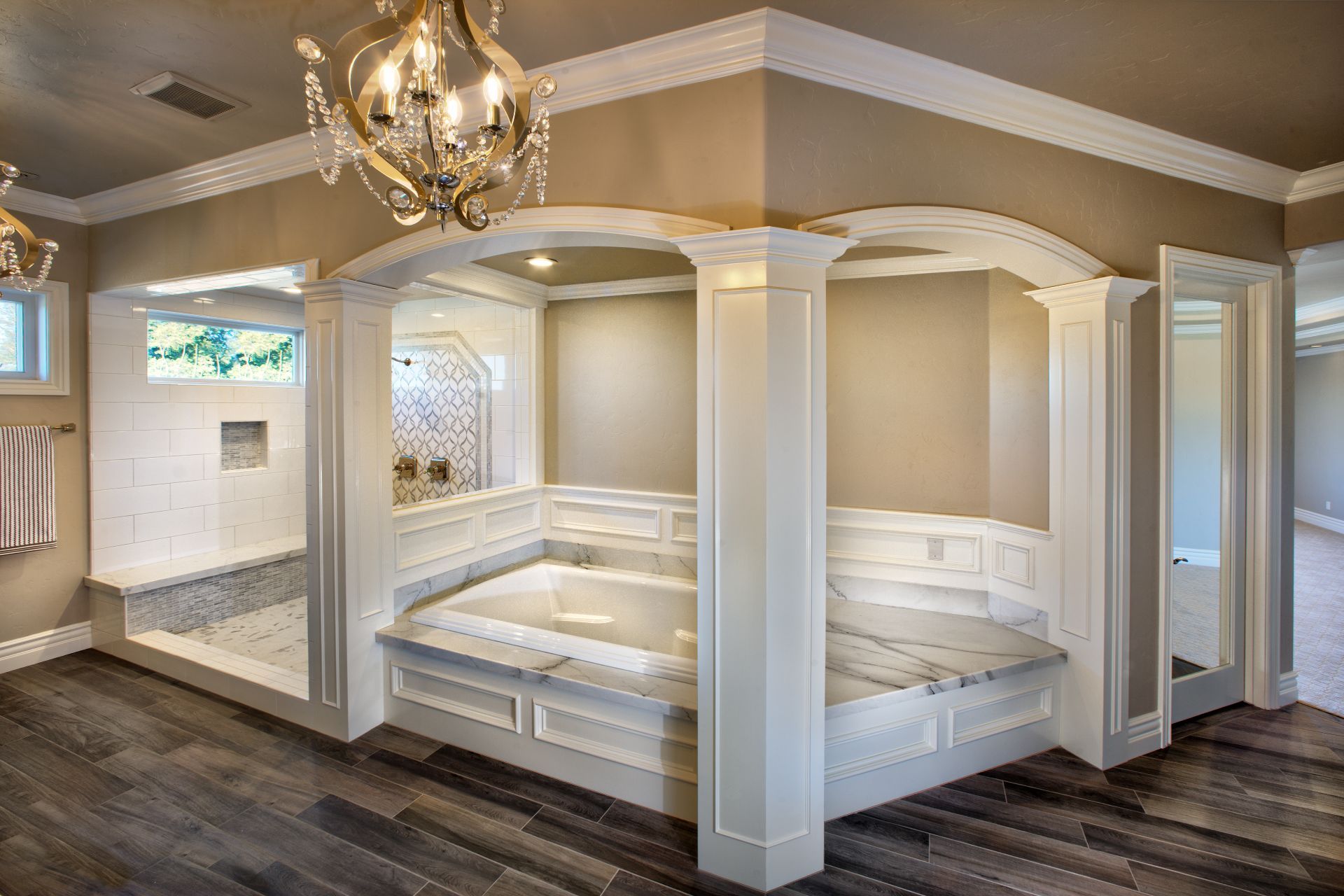 Luxury bathroom with a built-in tub and shower; cream walls, chandelier, and dark wood flooring.