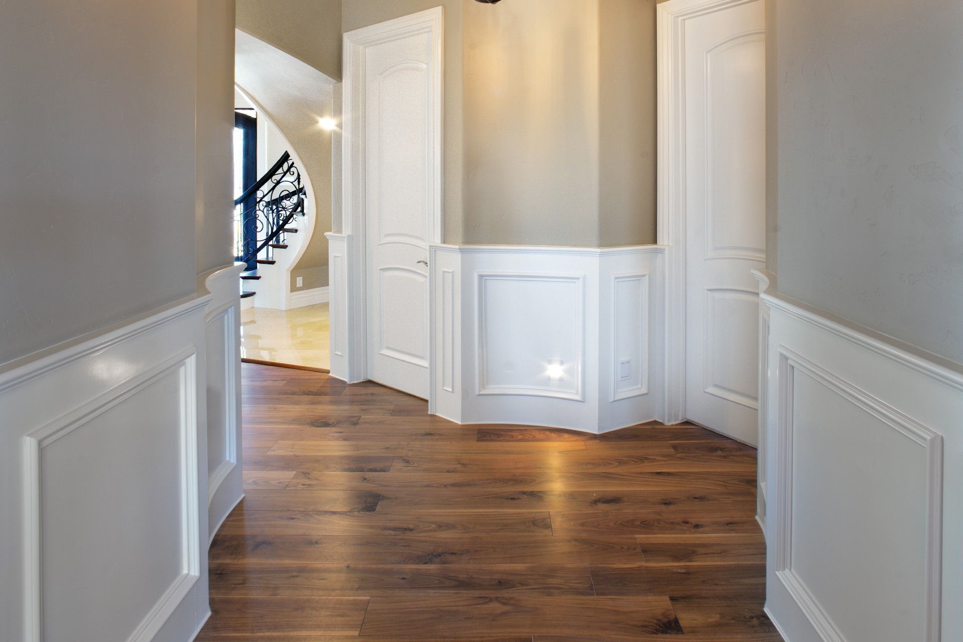 Hallway with wood floors, white paneling, and doors. Staircase visible in the background.