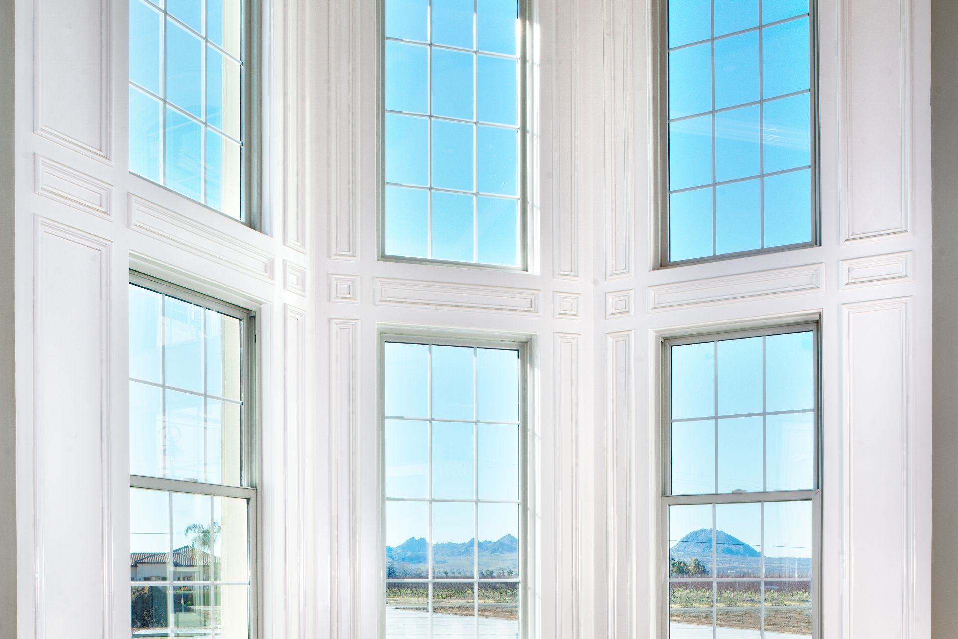 White-walled room with six large windows looking out at a bright blue sky and mountains.
