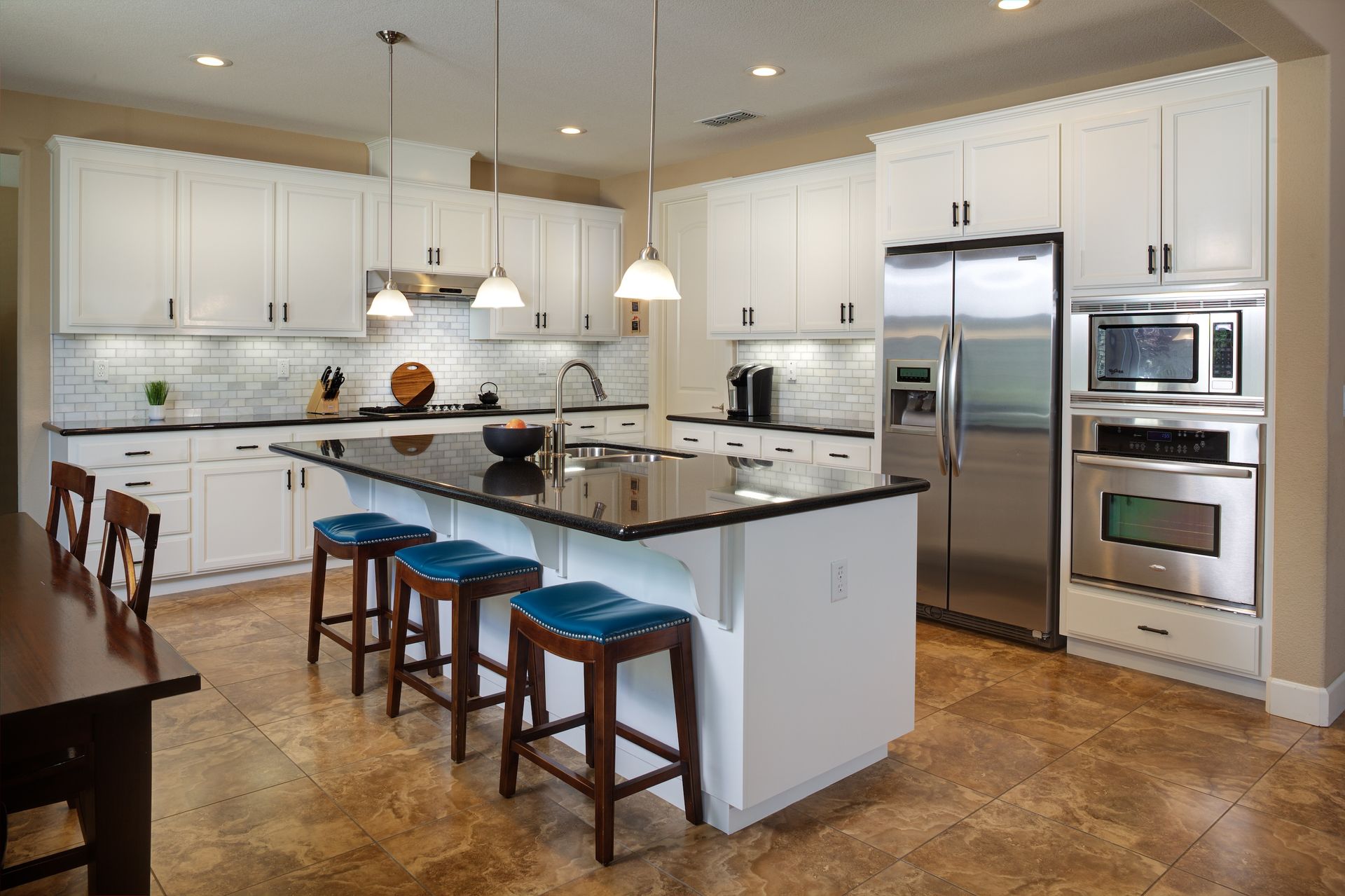 White kitchen with dark island, stainless steel appliances, and blue stools.