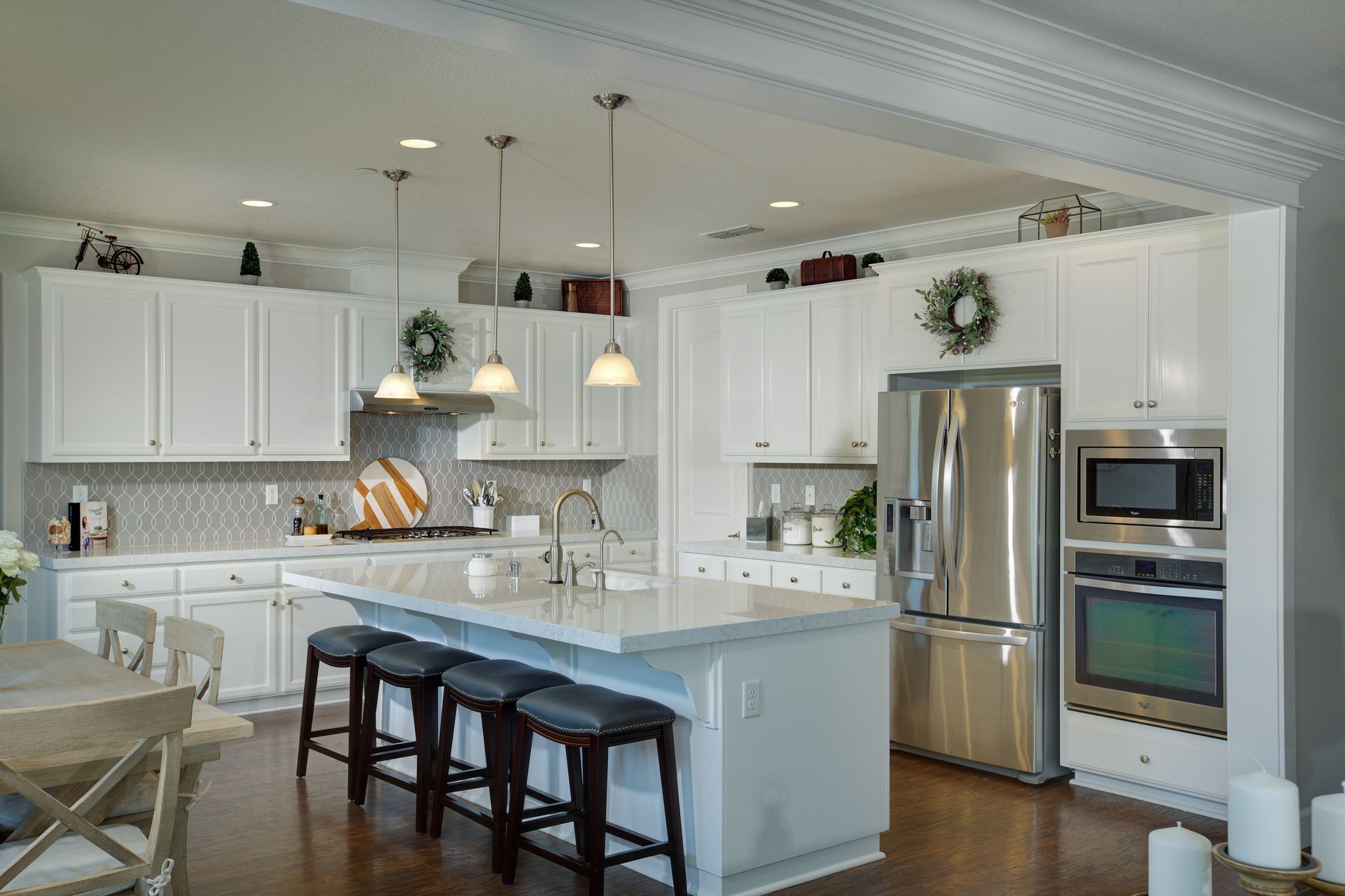 White kitchen with island, stainless steel appliances, and pendant lights.