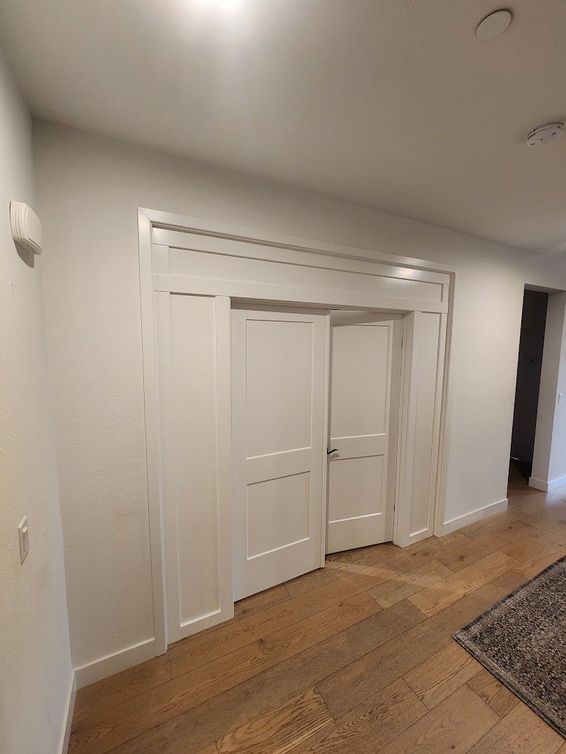 White double closet doors in a hallway with wood floors and a rug on the right.