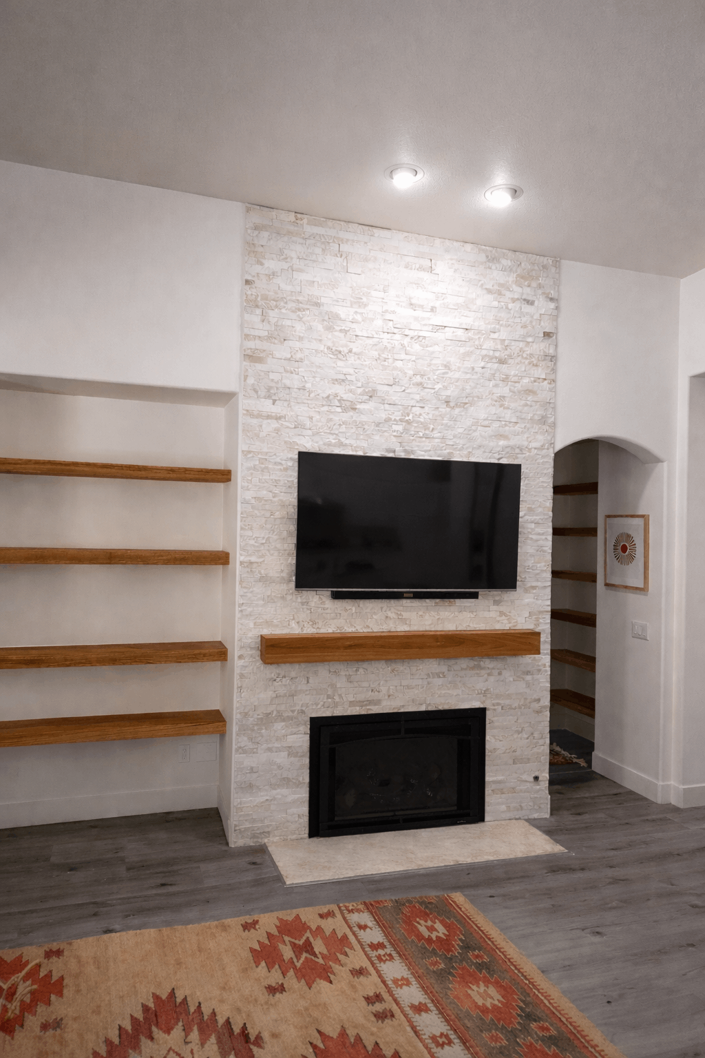 Living room with a fireplace, TV, built-in shelves, and a rug. Stone wall and wood accents.