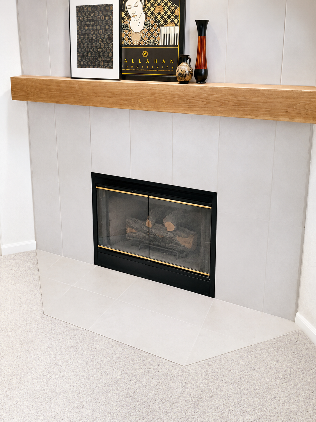 Modern fireplace with white tile surround, wooden mantel, and decorative items on top.