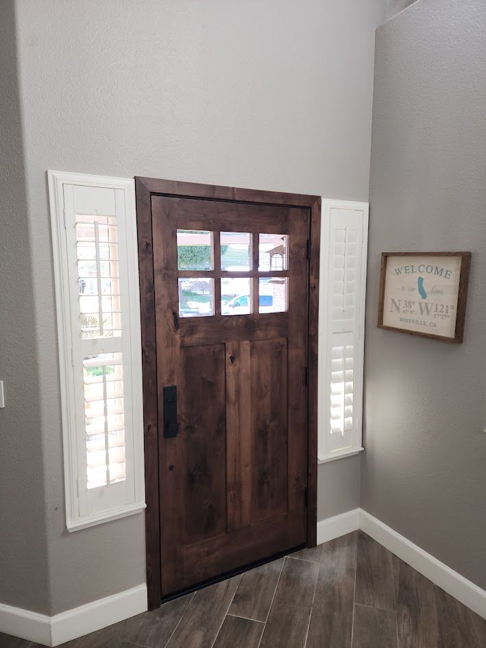 Front door with glass panes, flanked by sidelights, on a gray stucco porch with a welcome mat and decorative sign.
