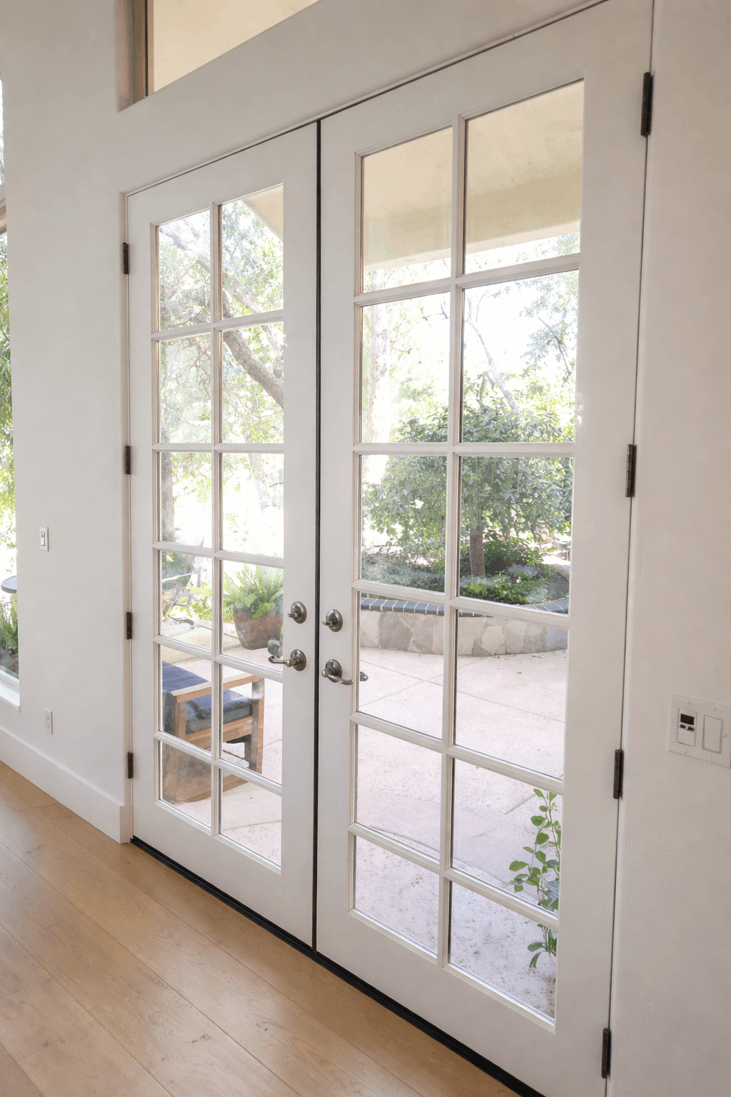 White French doors open to a patio with greenery.
