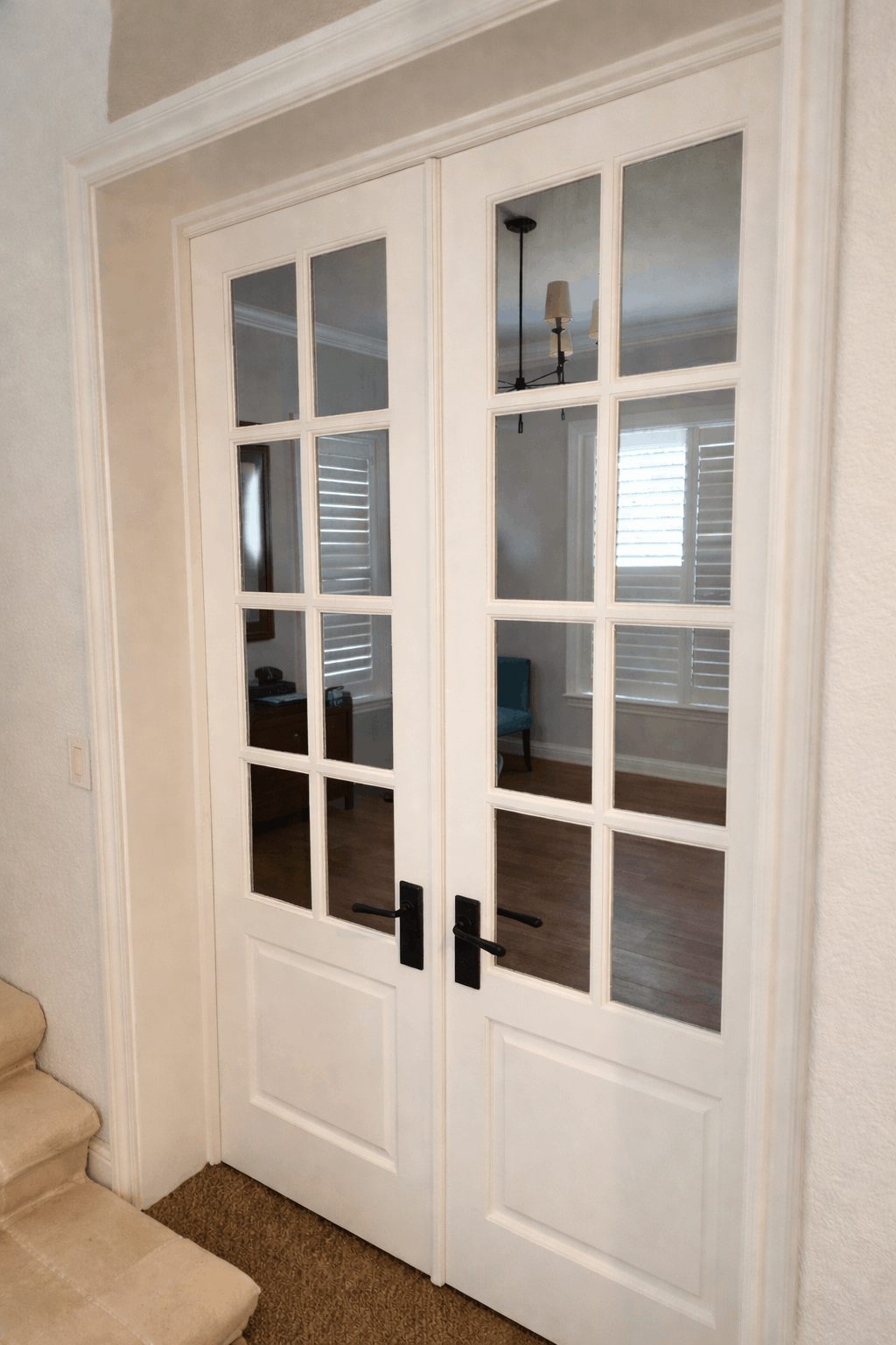 White French doors with glass panes, black handles, set in a white doorway.