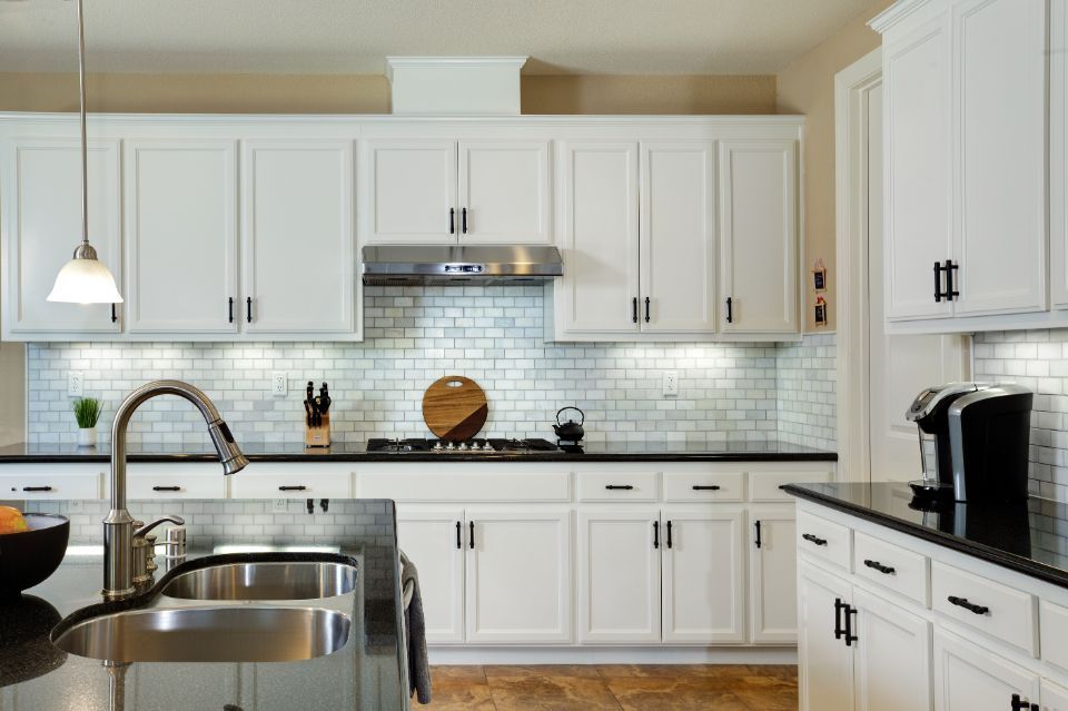 White kitchen with black countertops, white cabinets, subway tile backsplash, stainless steel appliances.