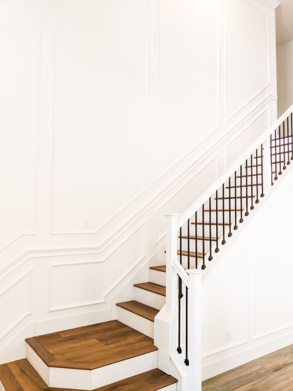 Staircase with wood steps, white walls, and black railing.