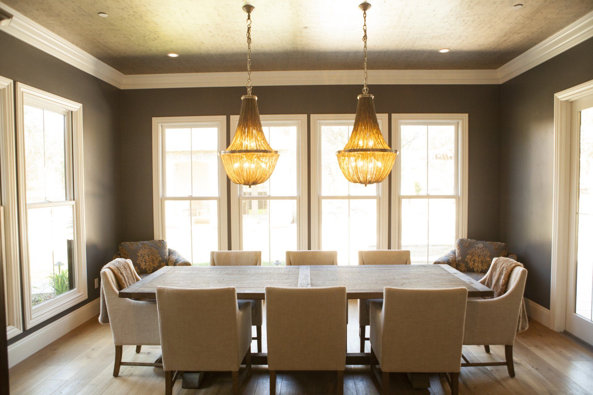 Elegant dining room with a large table, chairs, and chandelier lighting. Windows provide natural light.